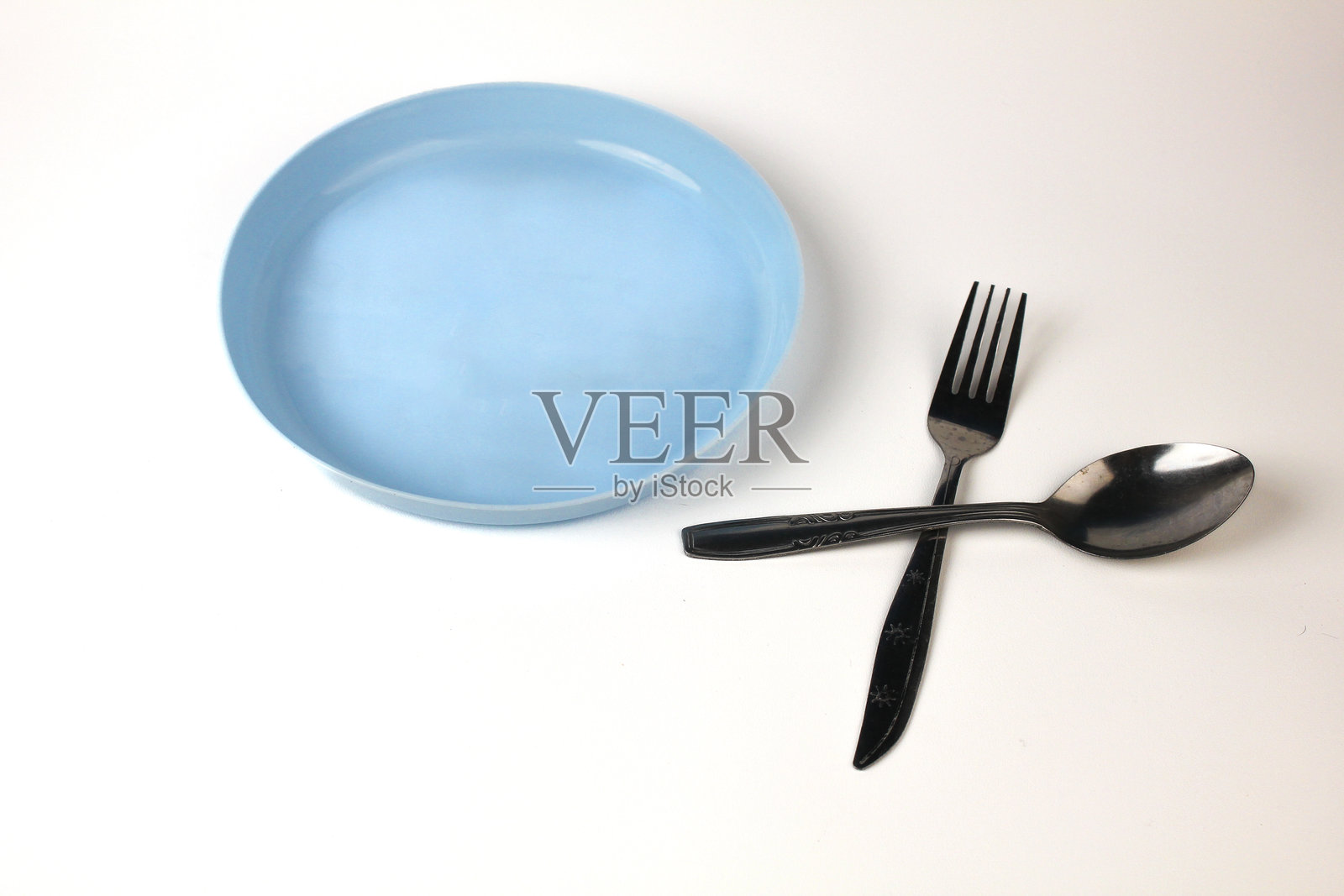 蓝色的塑料盘子、勺子和叉子，在白色背景上孤立。一套极简风格的家用刀叉餐具照片摄影图片