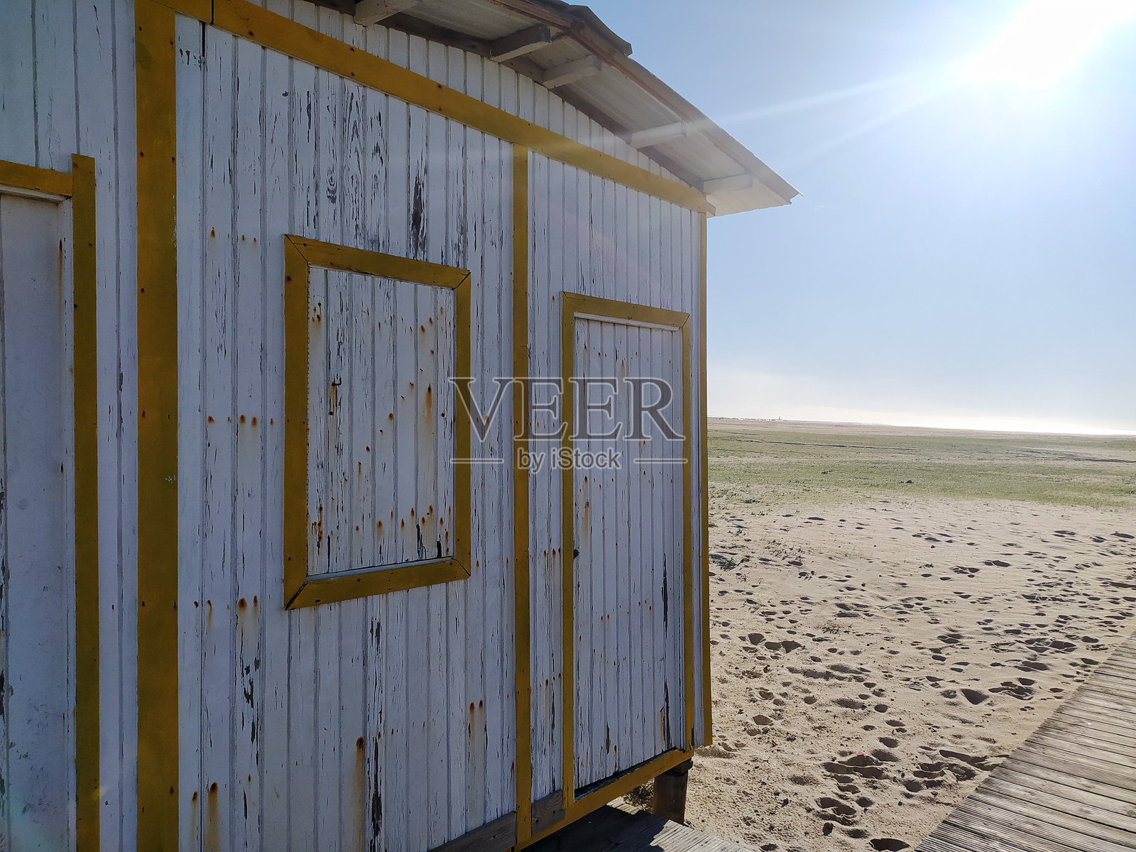 阳光沐浴、饱经风霜的海滩小屋，饰有黄色镶边，坐落在沙滩上。这是海岸独处和怀旧的质朴象征，非常适合夏季旅游博客和海滨生活方式项目。照片摄影图片