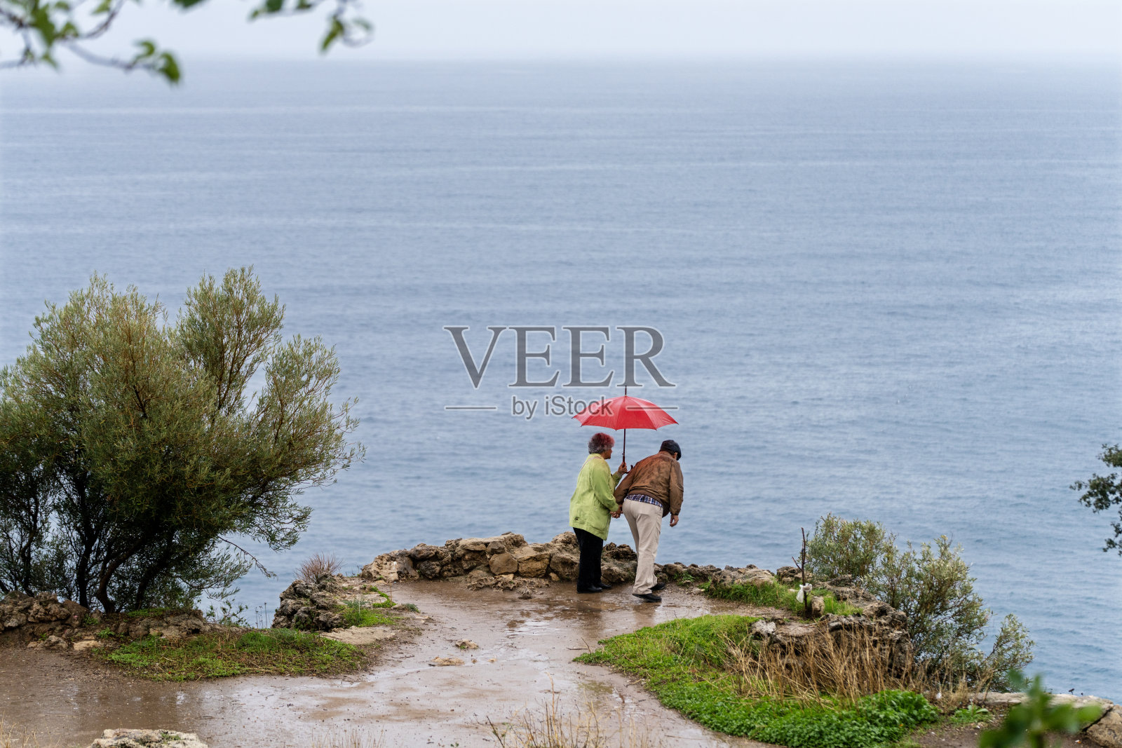 一对老年夫妇在户外的湿漉漉的小路上撑伞散步照片摄影图片