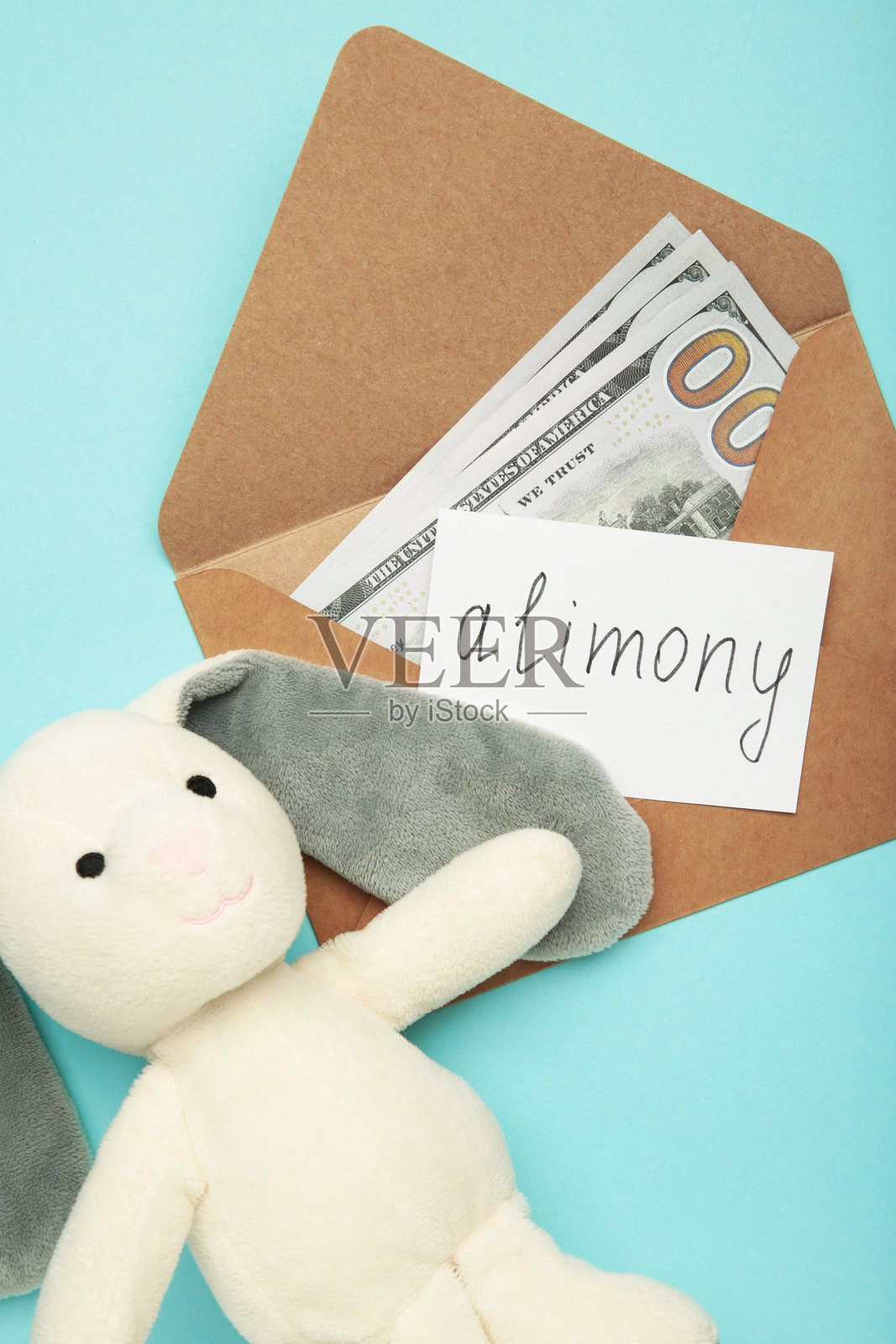 玩具兔子和写有“赡养费”字样及钞票的信封，背景为蓝色。竖幅照片照片摄影图片