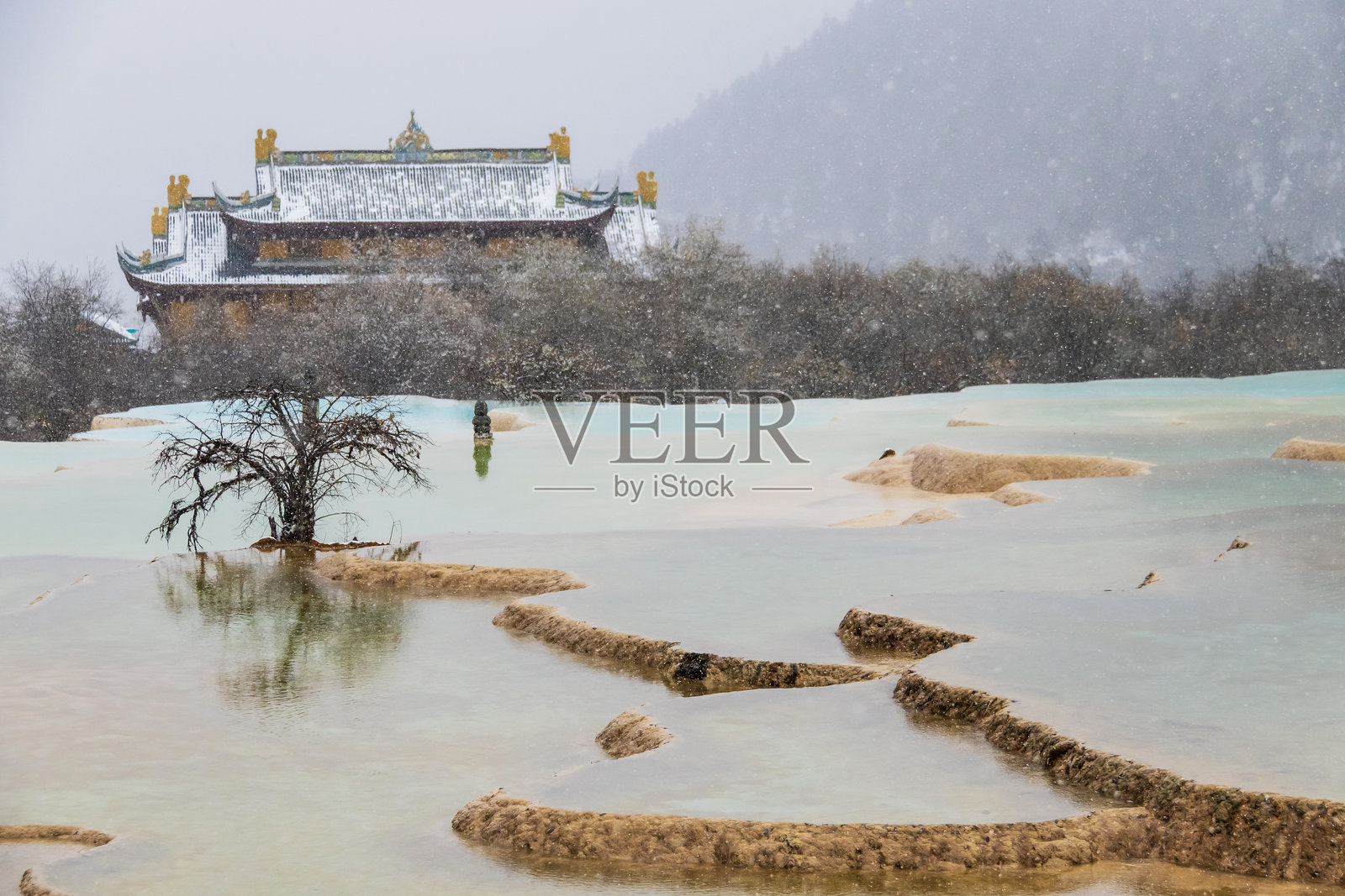 中国四川省黄龙国家公园的雪景寺庙露台，拥有绿松石色的钙华池和倒映在水中的孤树，这是一个宁静的冬季景观，也是一个联合国教科文组织世界遗产地。照片摄影图片
