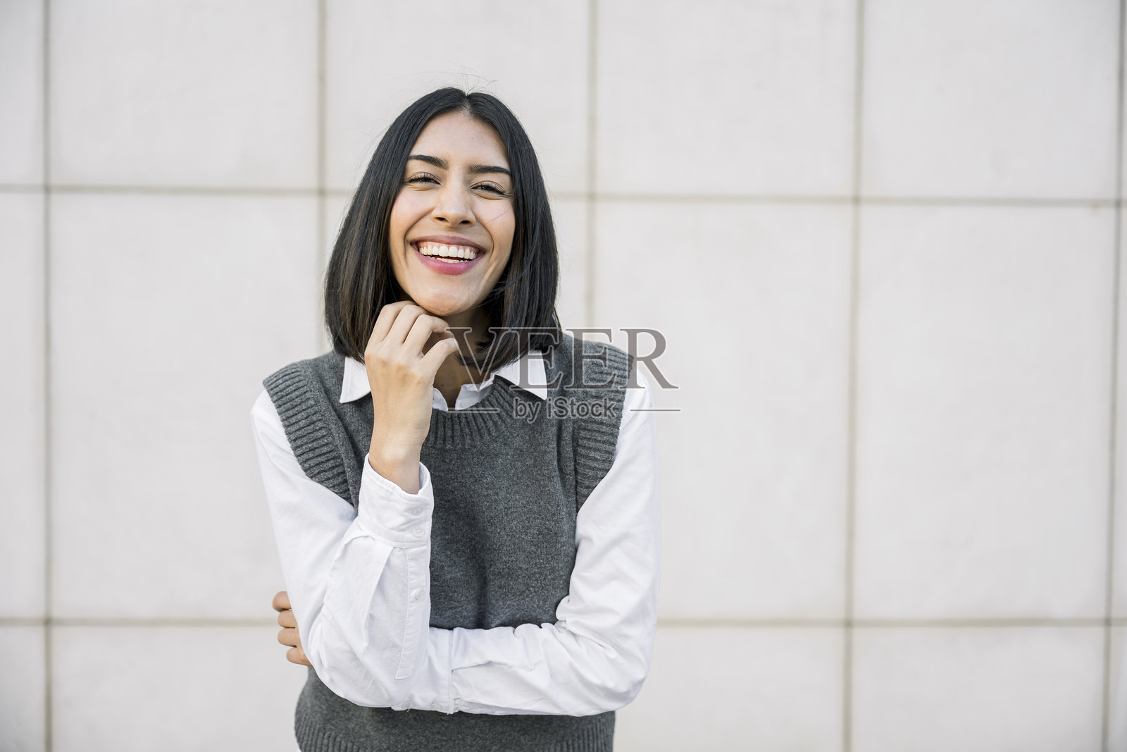 年轻女子对着纯色都市墙壁微笑、大笑照片摄影图片