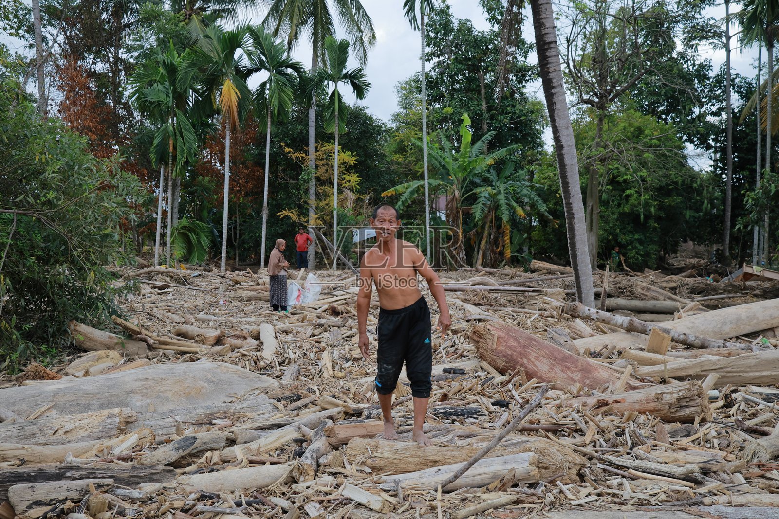2025年12月21日，在亚齐省皮迪贾亚，居民们在山洪暴发和山体滑坡后，走过木梁和泥泞的地面。照片摄影图片