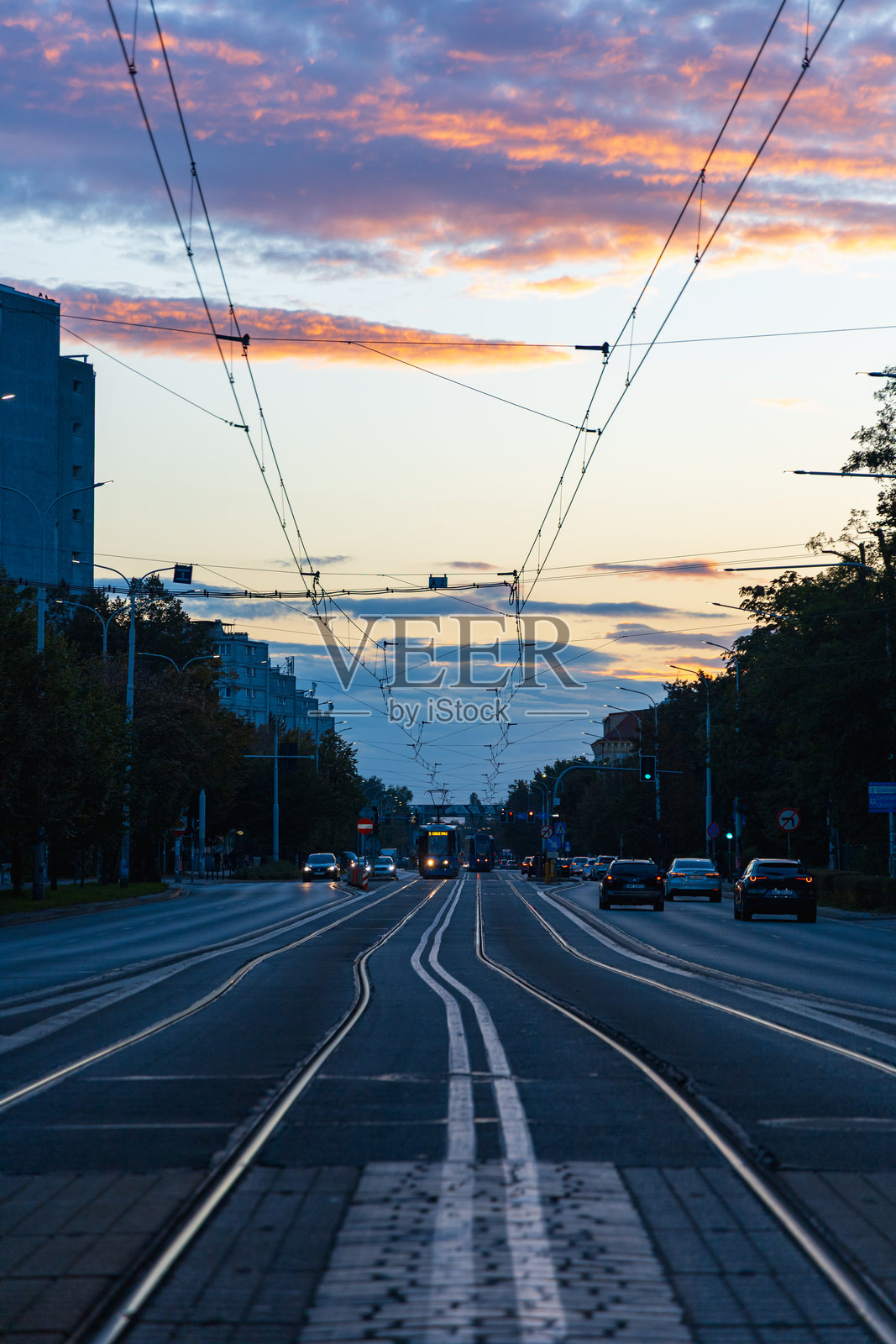 日落时分的城市街道,有电车轨道和驶过的电车,捕捉了夜晚的城市交通、架空电缆和充满活力的天空色彩照片摄影图片