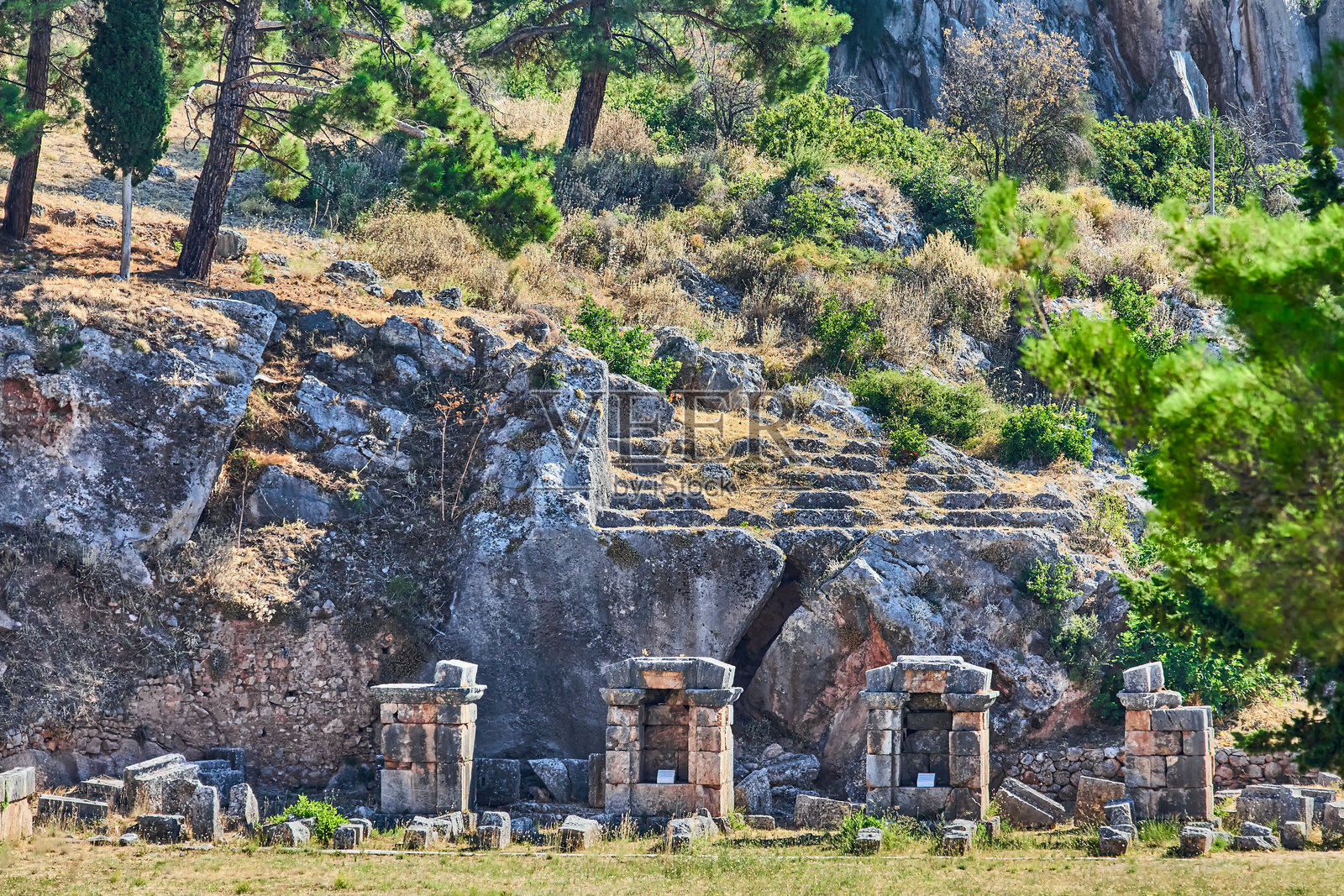 古老的石墙，墙上有一个凹进的壁龛，壁龛内立着一根顶端带有柱头的石柱。墙体由不同尺寸的红褐色砖石砌成，位于希腊中部德尔斐。照片摄影图片