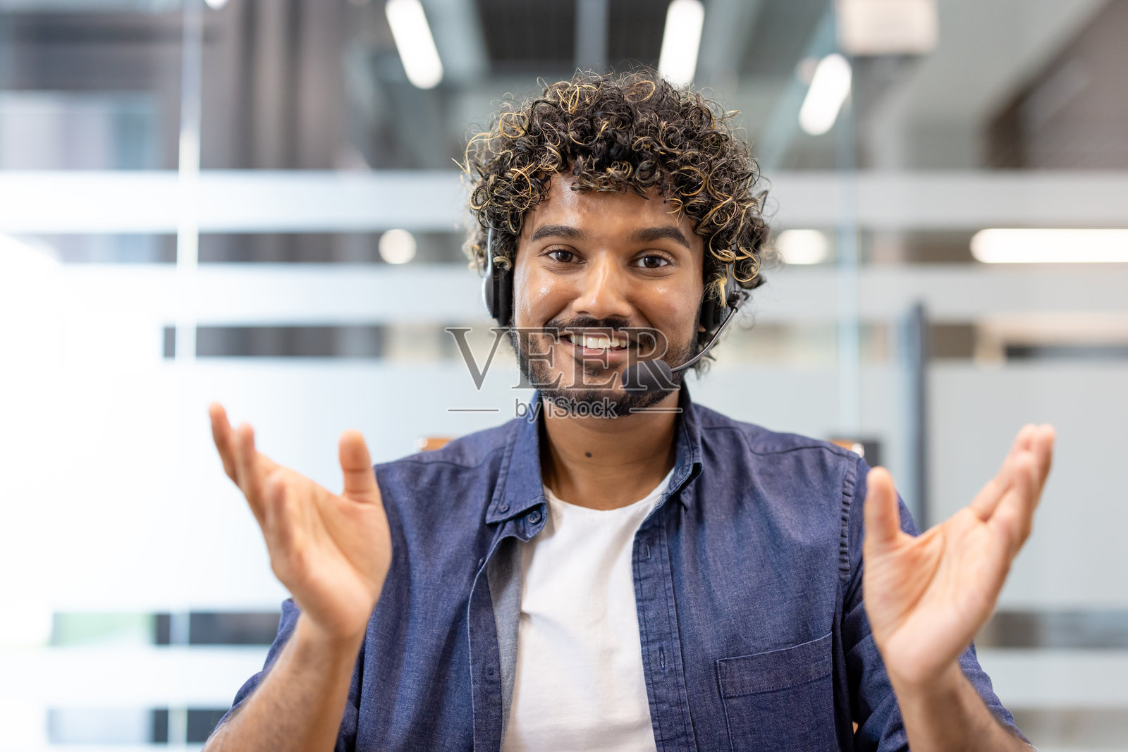 一位年轻的印度男子戴着耳机，面带微笑，在办公室里对着镜头拍摄肖像照照片摄影图片