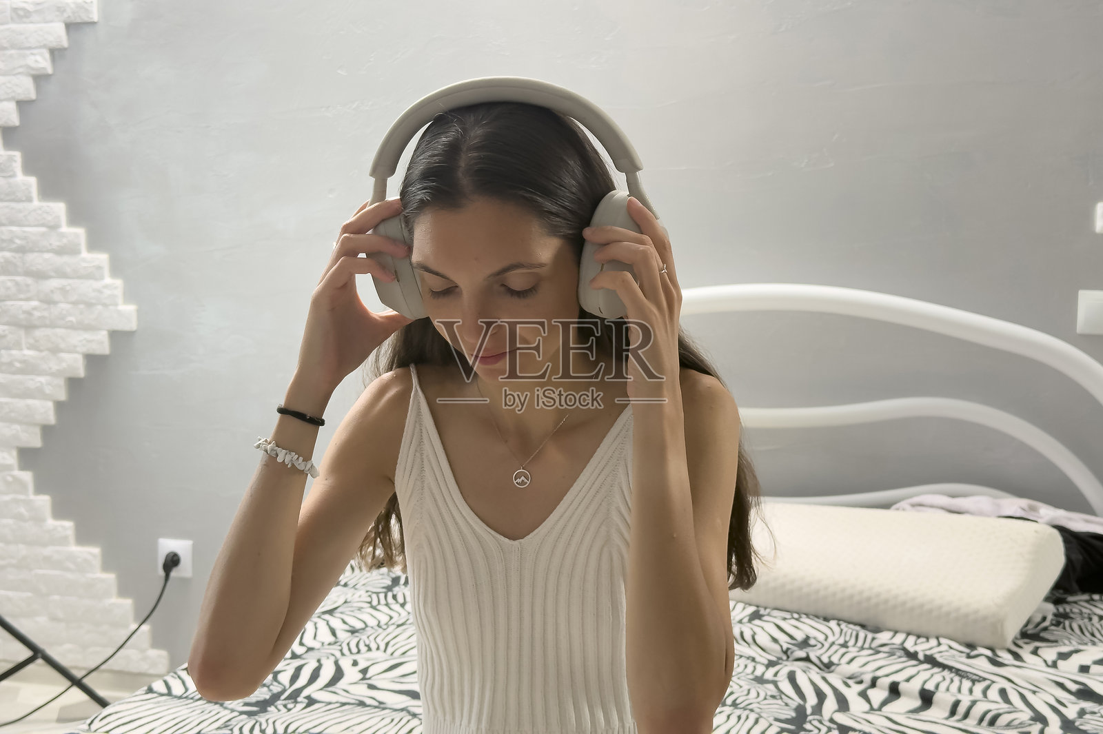 女子坐在床上，一边调整耳机一边听音乐照片摄影图片