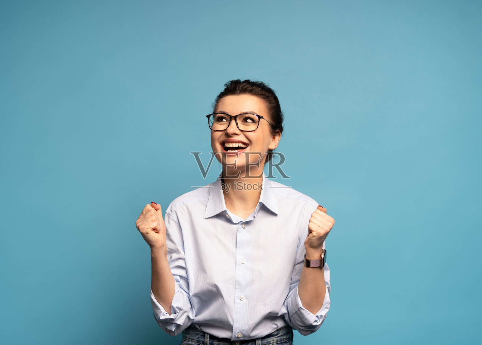 一名非常开心的女子，高举握紧的拳头站立，像是中了彩票，庆祝成功，孤立在蓝色背景上照片摄影图片