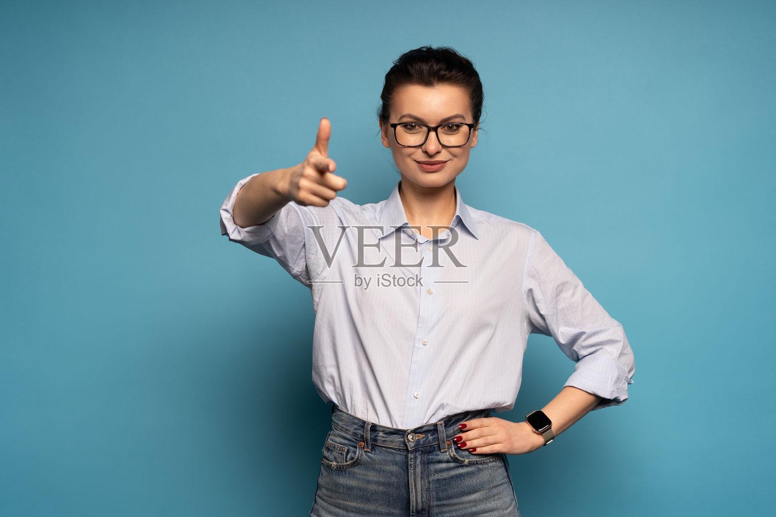 身穿蓝色T恤、戴着眼镜的职业女性，伸出食指指向镜头，鼓励和激励观众，孤立在蓝色背景上照片摄影图片
