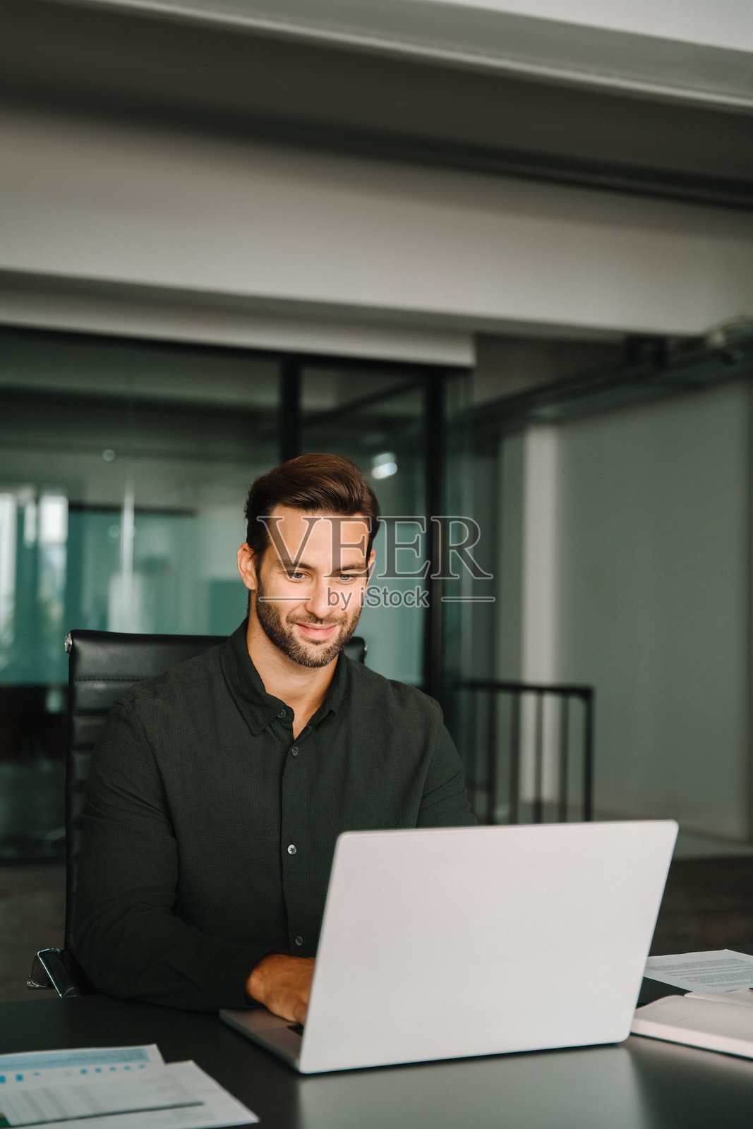 30多岁的拉丁裔年轻商务男士在公司办公室使用笔记本电脑工作。微笑的欧洲企业家经理商务人士使用电脑进行沟通、在工作场所学习。竖图，有复制空间照片摄影图片