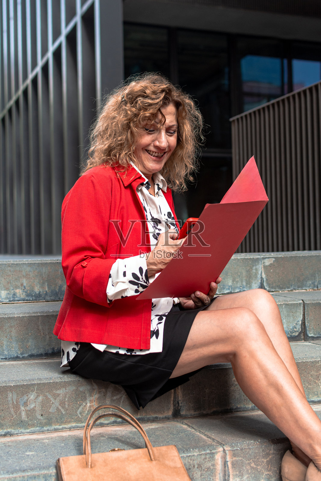 女商人坐在城市台阶上，一边查看文件一边使用手机照片摄影图片