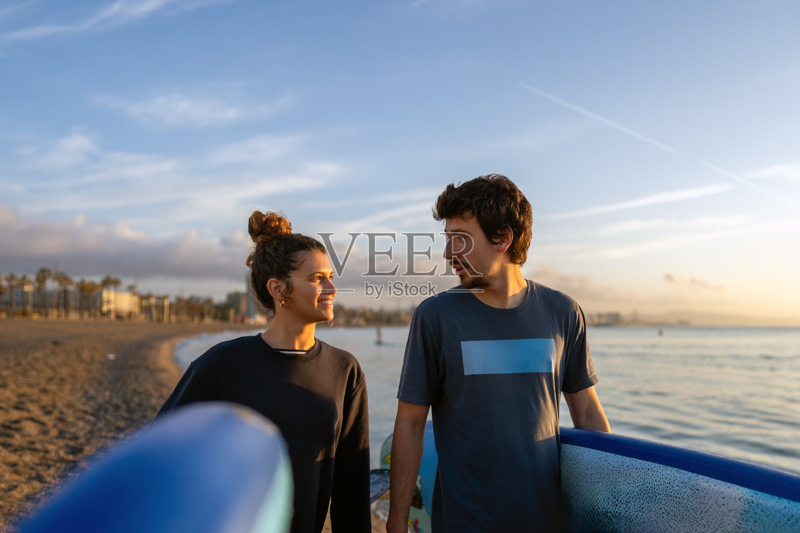 朋友们在日落时分的海滩上分享欢乐时刻，他们笑着拿着色彩鲜艳的冲浪板照片摄影图片