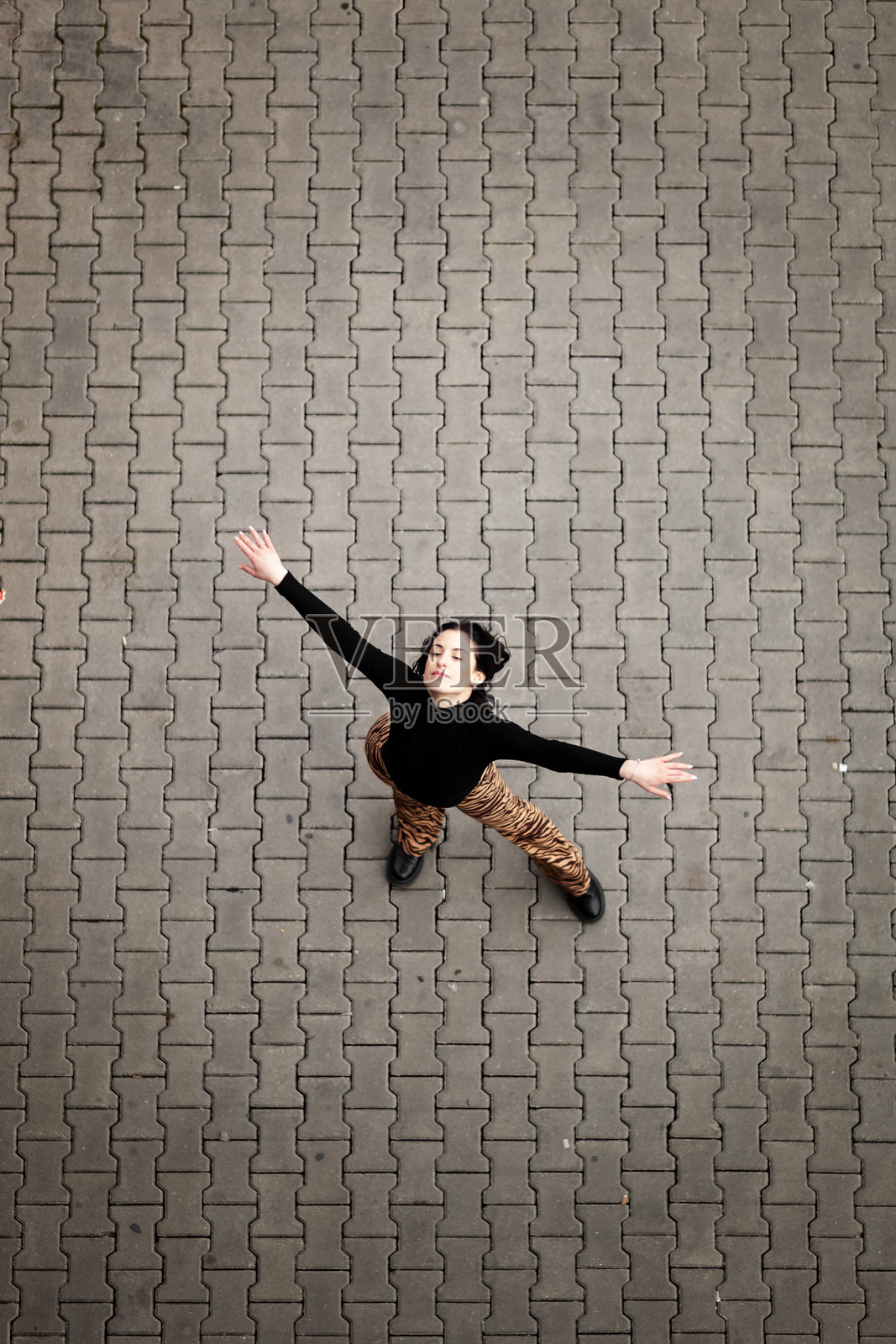 一个阳光明媚的下午，在城市里，一个女孩张开双臂，精神焕发地在鹅卵石人行道上快乐地跳舞照片摄影图片