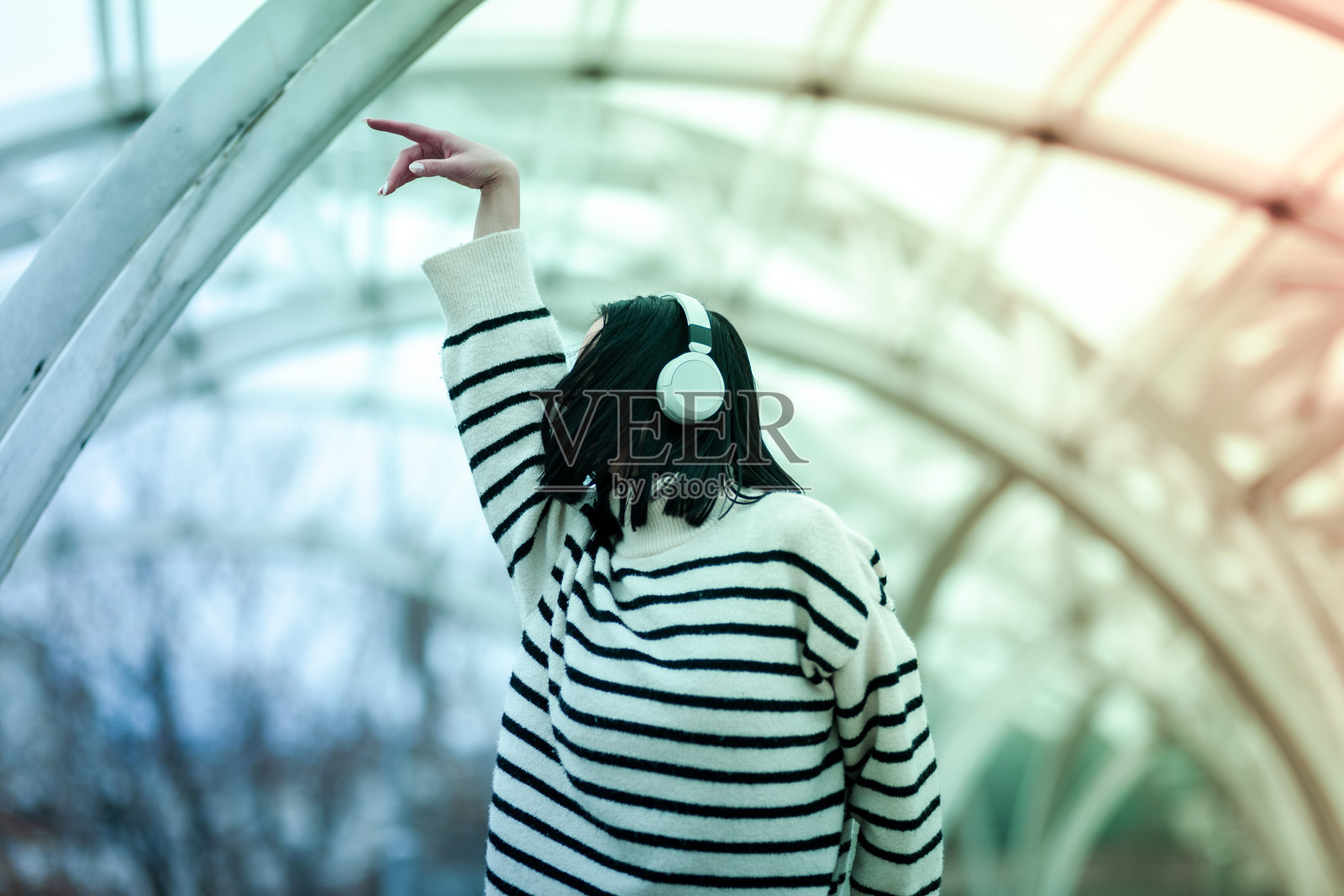 一个明亮的下午，女孩戴着耳机，在一个独特的城市弯曲结构下快乐地跳舞，享受着音乐。照片摄影图片