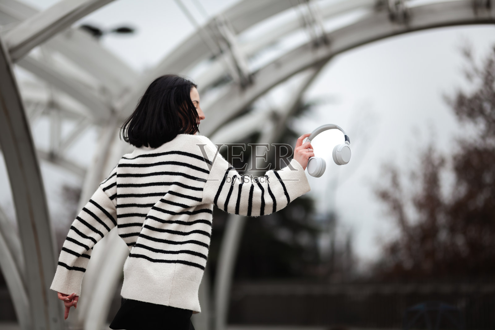 一个女孩在阴天时，在城市环境中快乐地跳舞，手里拿着耳机，展现了她对音乐和运动的热爱照片摄影图片