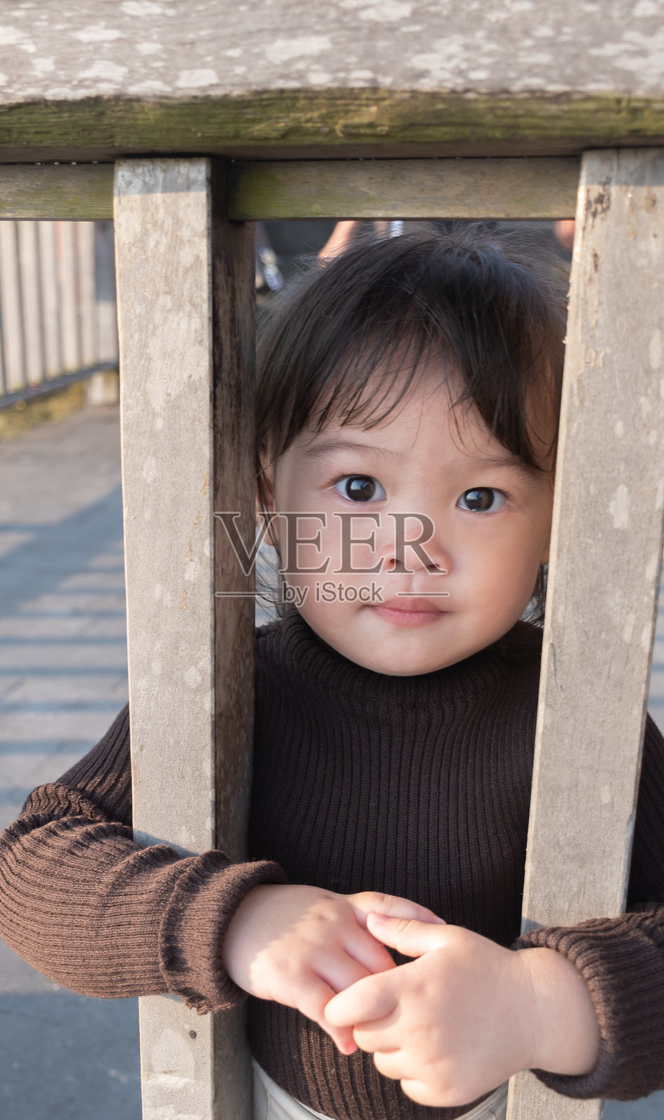 好奇的小女孩睁着大眼睛，从木栅栏的缝隙里偷看照片摄影图片