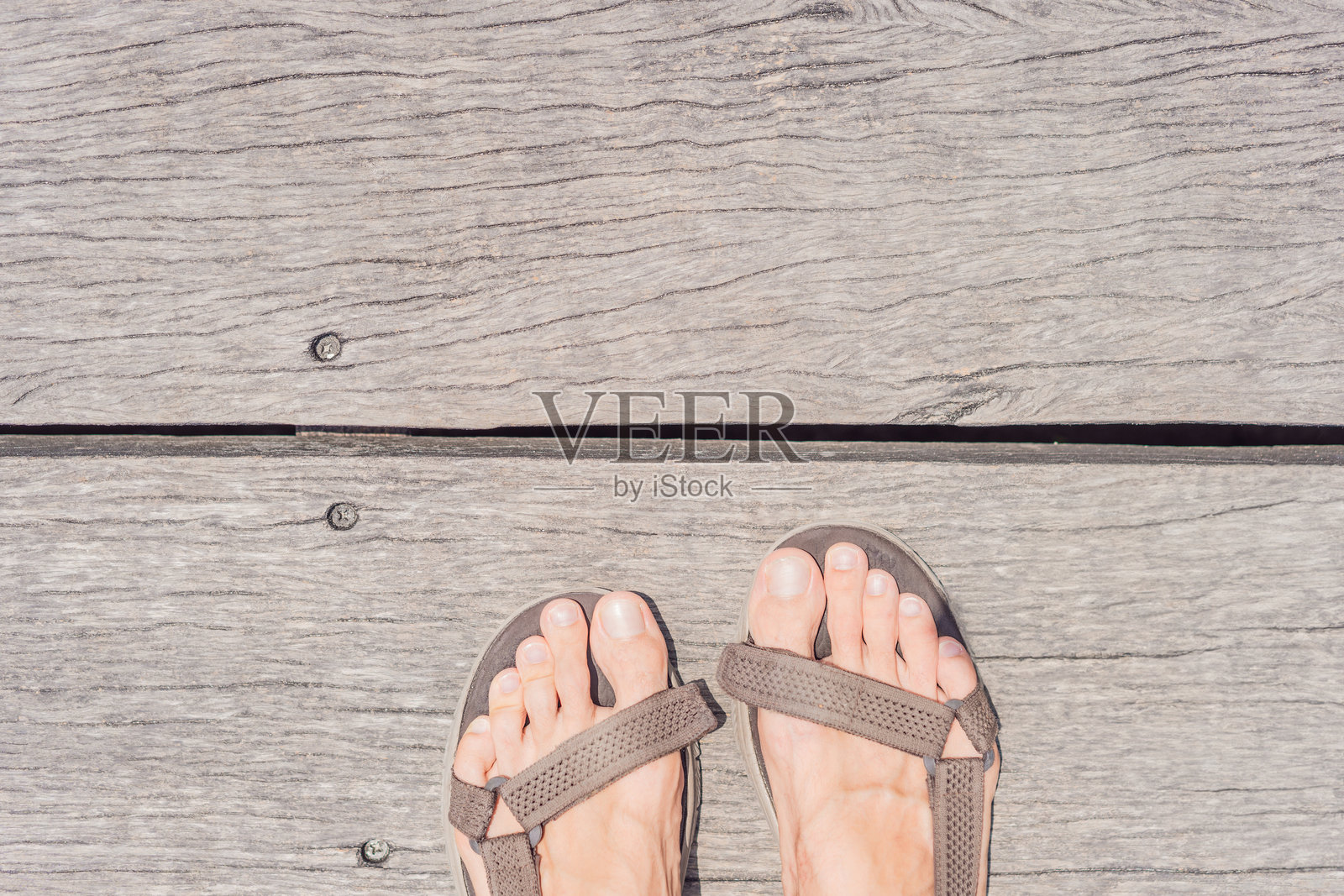 男人的腿搭在古老的木码头上，远处是风景如画的海滨景色。放松与旅行的概念照片摄影图片