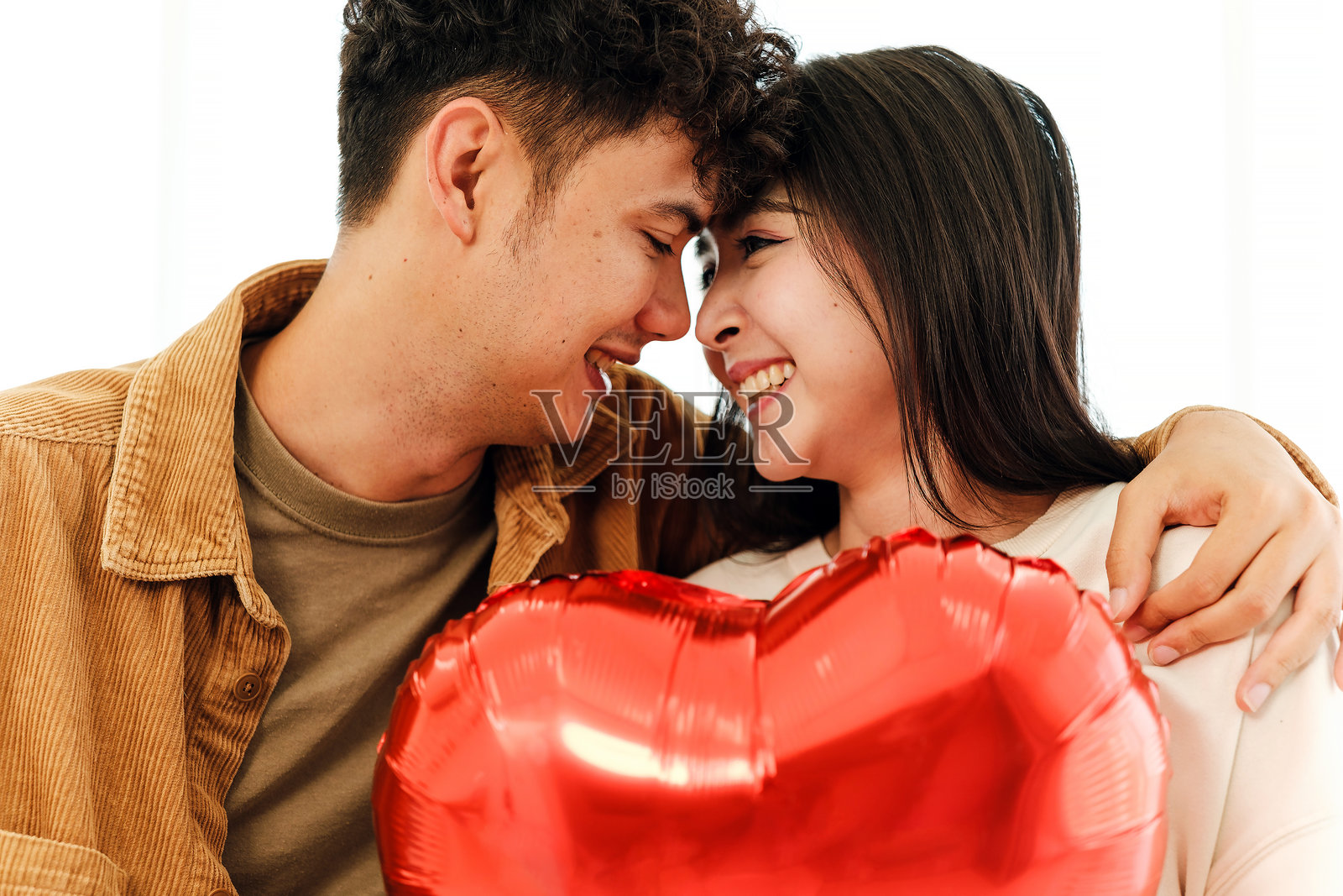 一对快乐的情侣拥抱着一个红色的心形气球，脸上洋溢着爱意、浪漫和温暖，非常适合在情人节或一年中的任何时候庆祝爱情和连接。照片摄影图片