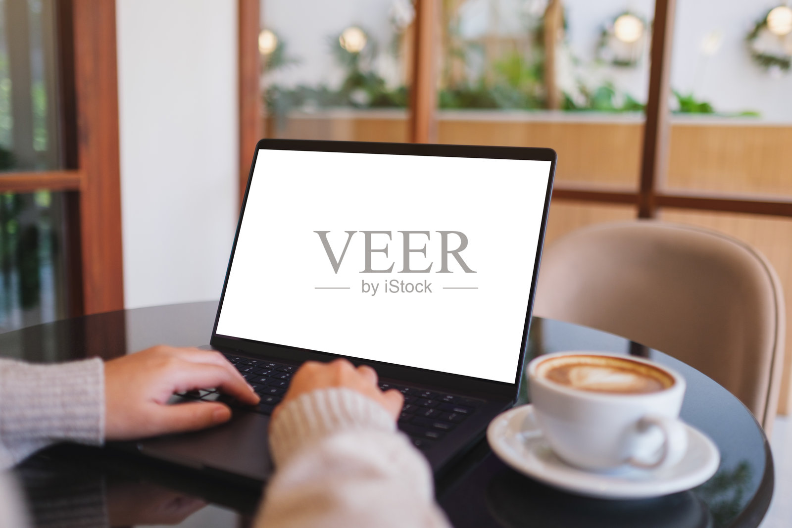 咖啡馆里，女子正在笔记本电脑上打字工作的样机图，屏幕为空白白色桌面。照片摄影图片