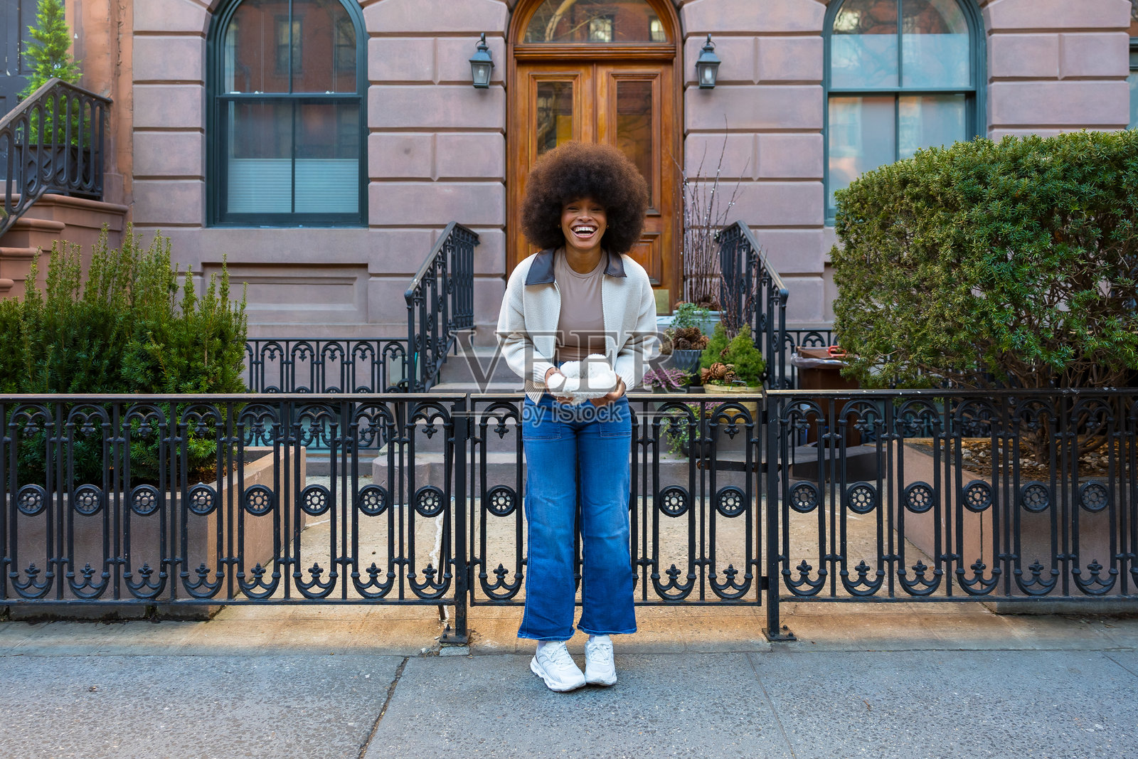 年轻女子微笑着，手里拿着白色毛线，背景是褐砂岩建筑照片摄影图片