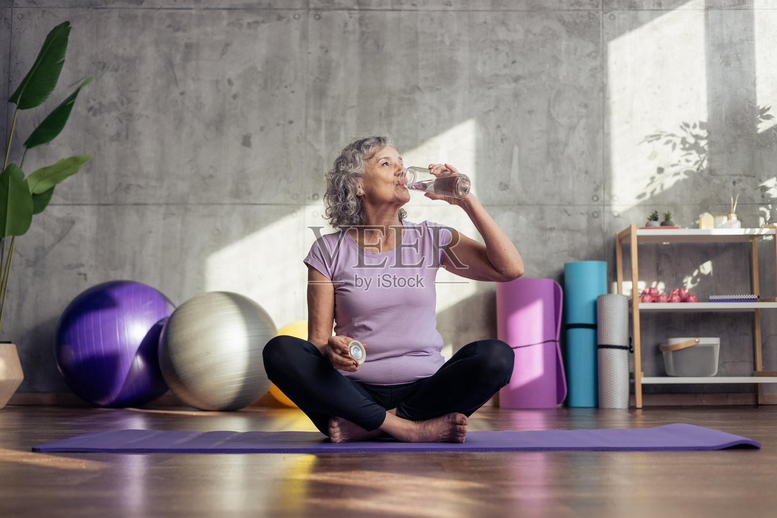 运动后在瑜伽垫上喝水的年长女性照片摄影图片