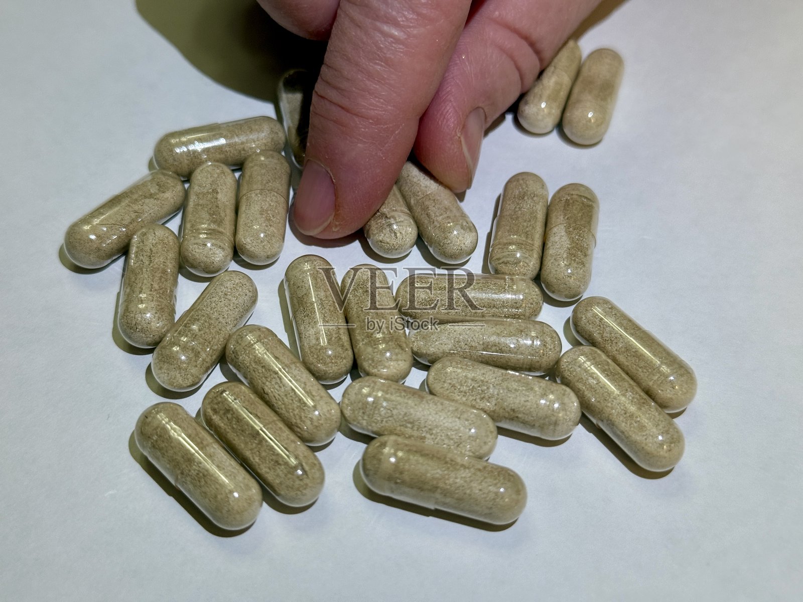草本胶囊整理，手指轻柔地分拣草本补充胶囊，特写手指在柔和光线下自然表面上精确排列米色草本补充剂照片摄影图片