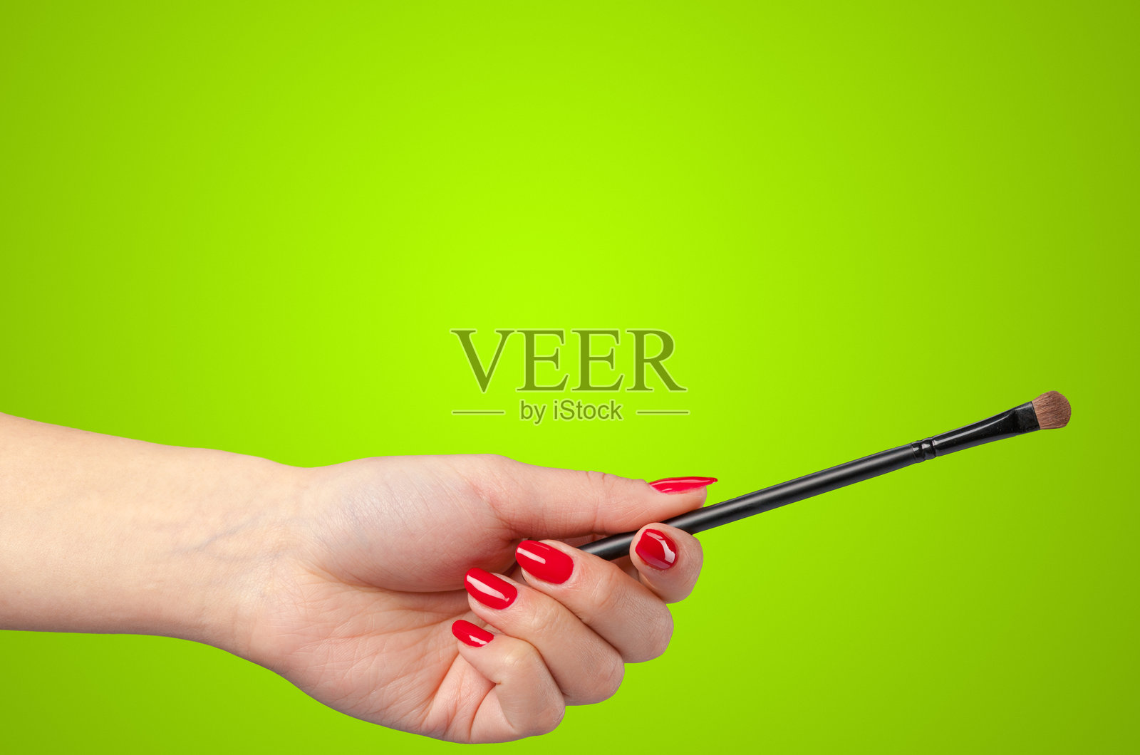 手持化妆刷，背景为亮绿色，置身于美容场景中照片摄影图片
