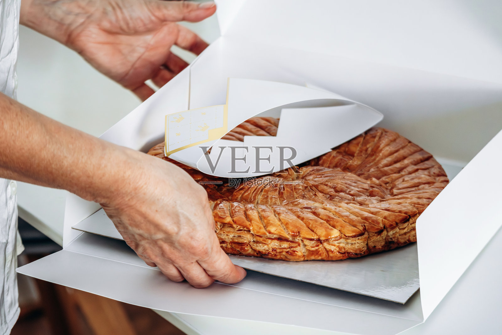 一位女子正在拆开国王饼（Galette des Rois），这是一种传统的法式酥皮点心，内馅是杏仁奶油，通常在一月份食用以庆祝主显节和三王来临。照片摄影图片