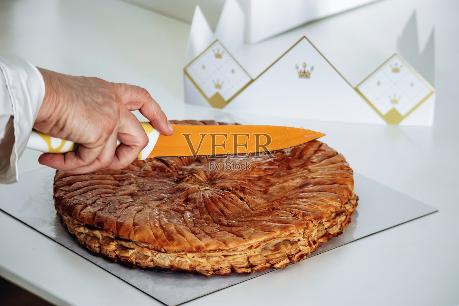 一位女士正在切割国王饼（Galette des Rois），这是一种传统的法式酥皮糕点，通常由酥脆的起酥皮和杏仁奶油制成，传统上在一月份分享以庆祝主显节和三王节。照片摄影图片