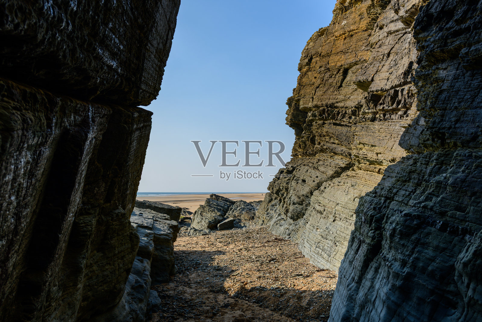 岩石海岸的裂缝通向沙滩照片摄影图片