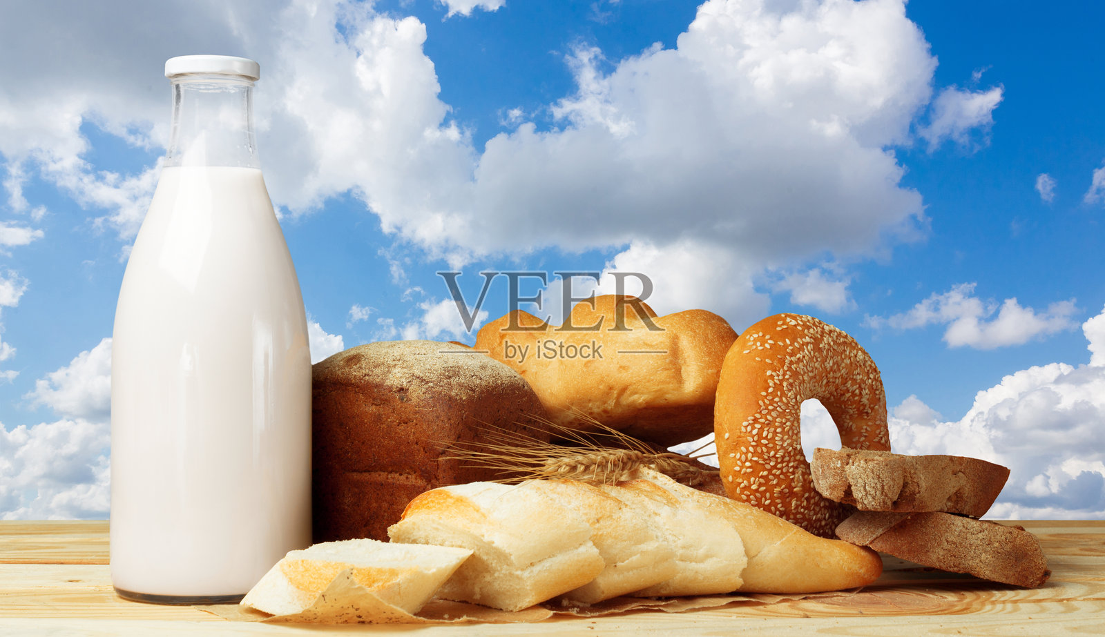 蓝天白云下，木桌上摆放着新鲜的面包和牛奶照片摄影图片