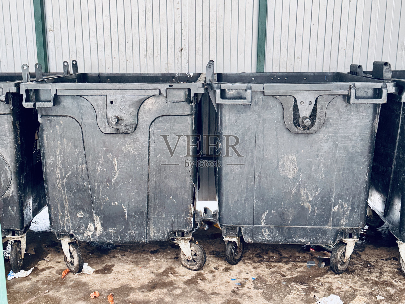 特写黑色垃圾箱，散落着垃圾，脚轮磨损，金属表面有油漆剥落和锈迹，服务区和潮湿路面粗糙的质感表明使用频繁照片摄影图片