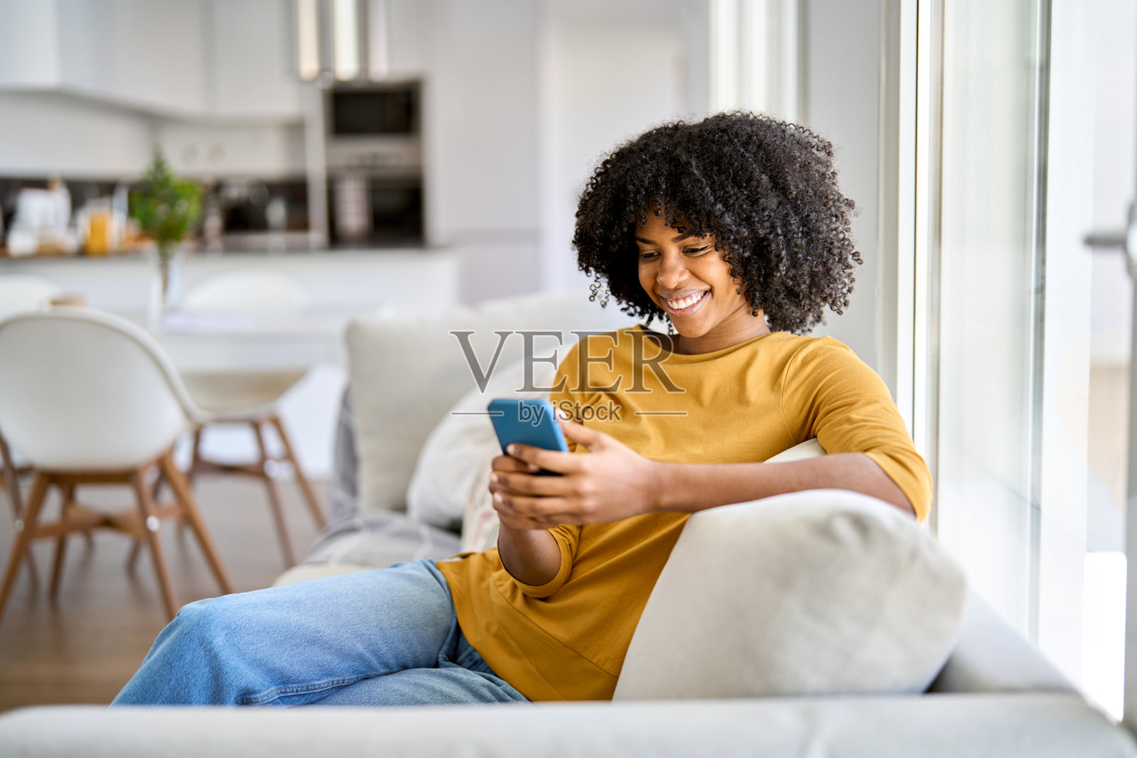 快乐的年轻非裔美国女性在家中沙发上使用手机。照片摄影图片