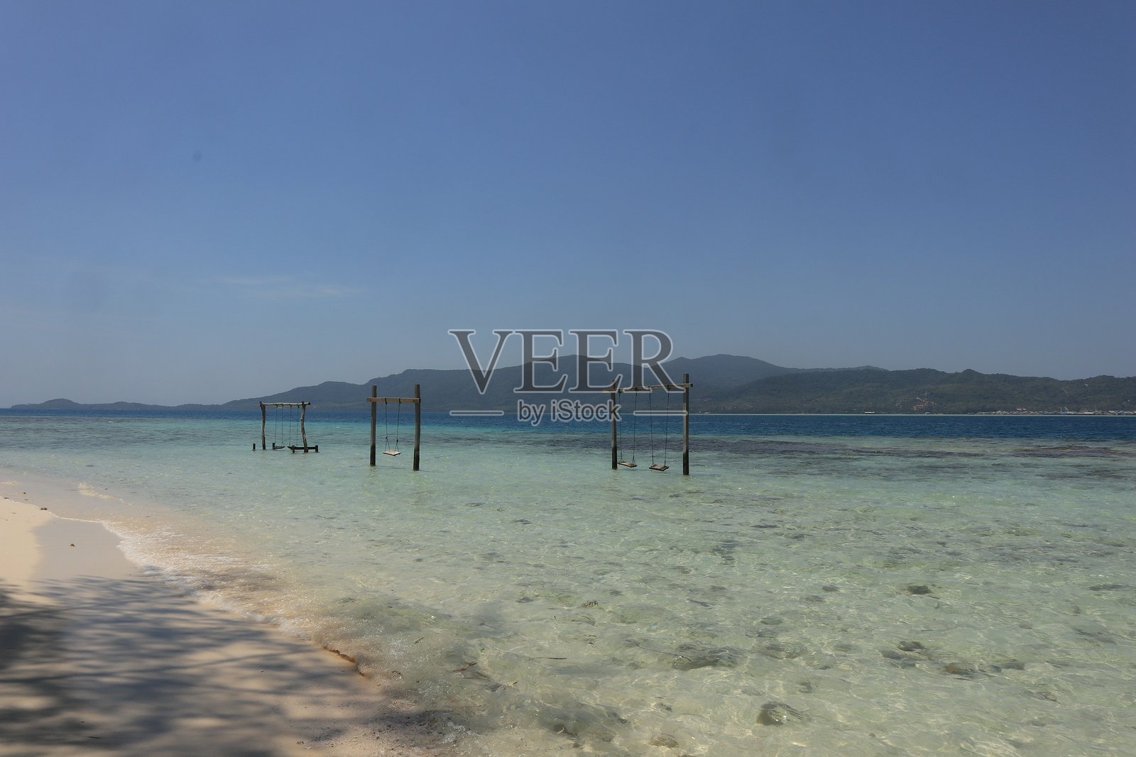 美丽的沙滩，拥有洁白的沙滩和停泊在清澈湛蓝海水中的传统船只，天空晴朗照片摄影图片