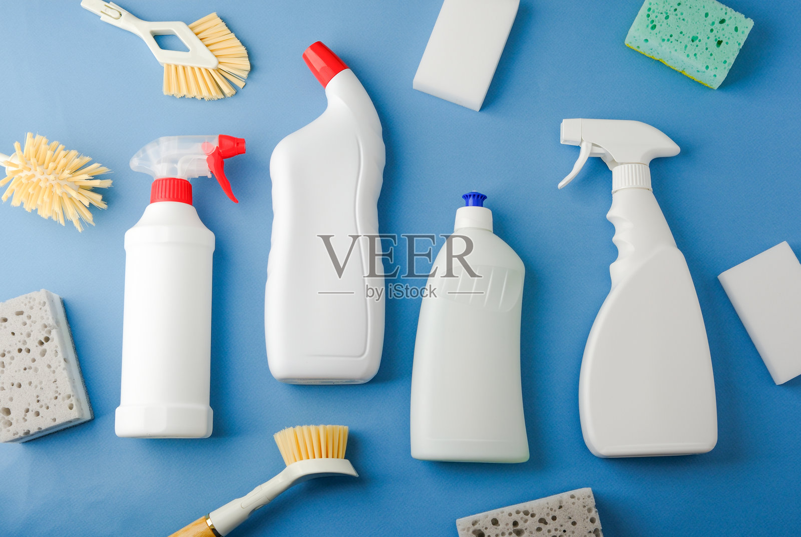 白色清洁瓶子、刷子和海绵在蓝色表面上排列照片摄影图片