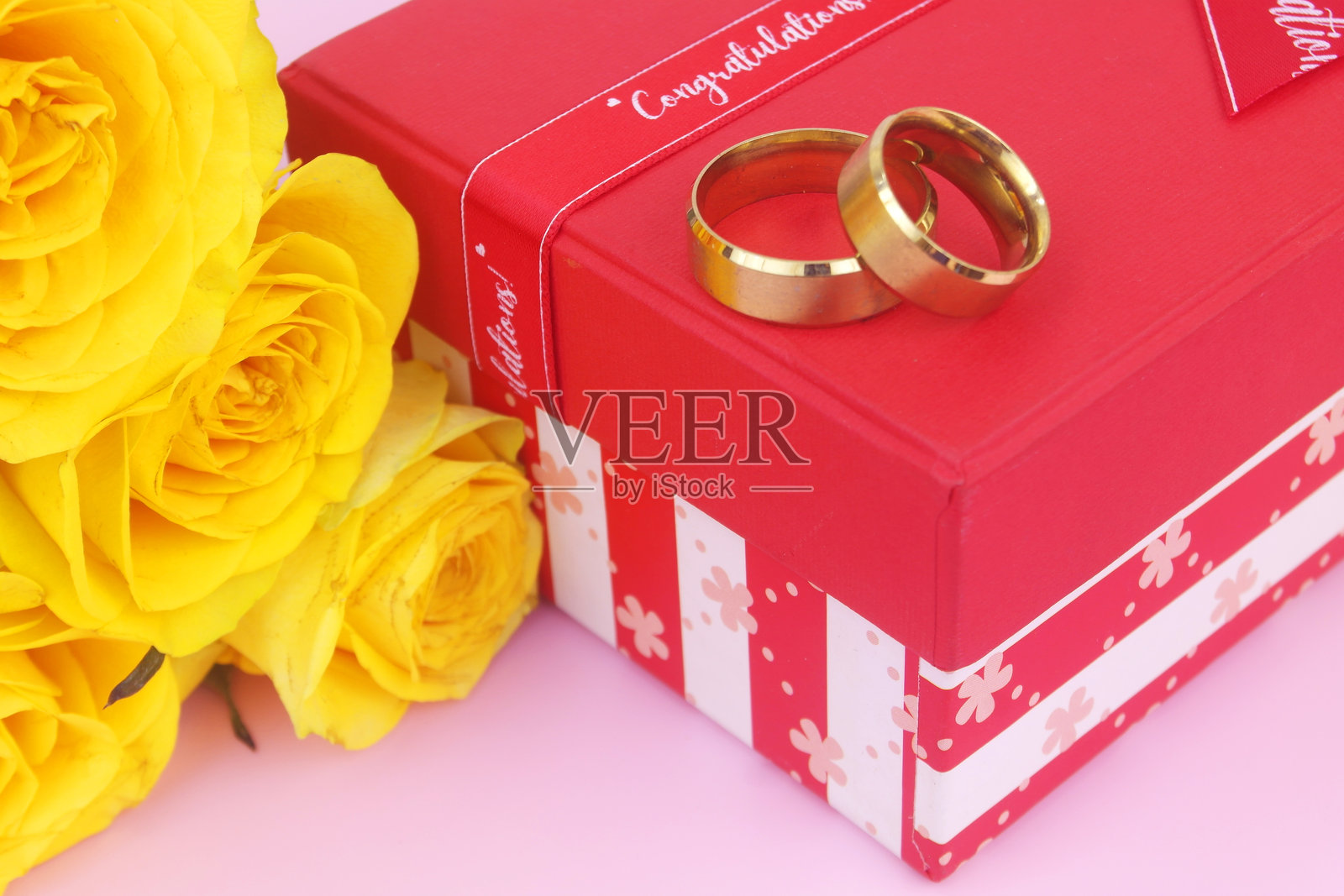 粉色背景上的黄色玫瑰花束，配有金色婚戒和礼品盒。照片摄影图片