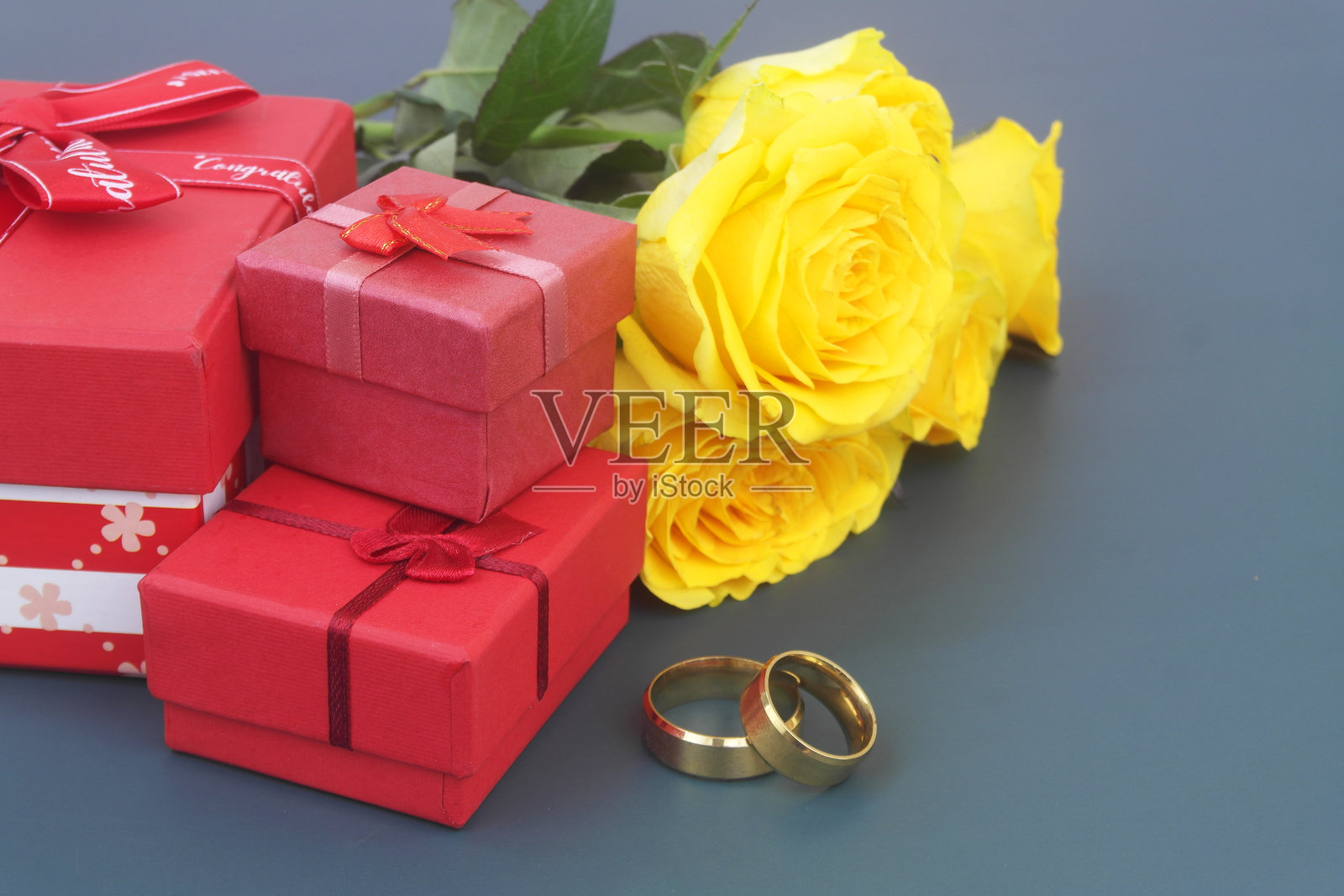 蓝底上带有金色婚戒和礼品盒的黄色玫瑰花束。照片摄影图片