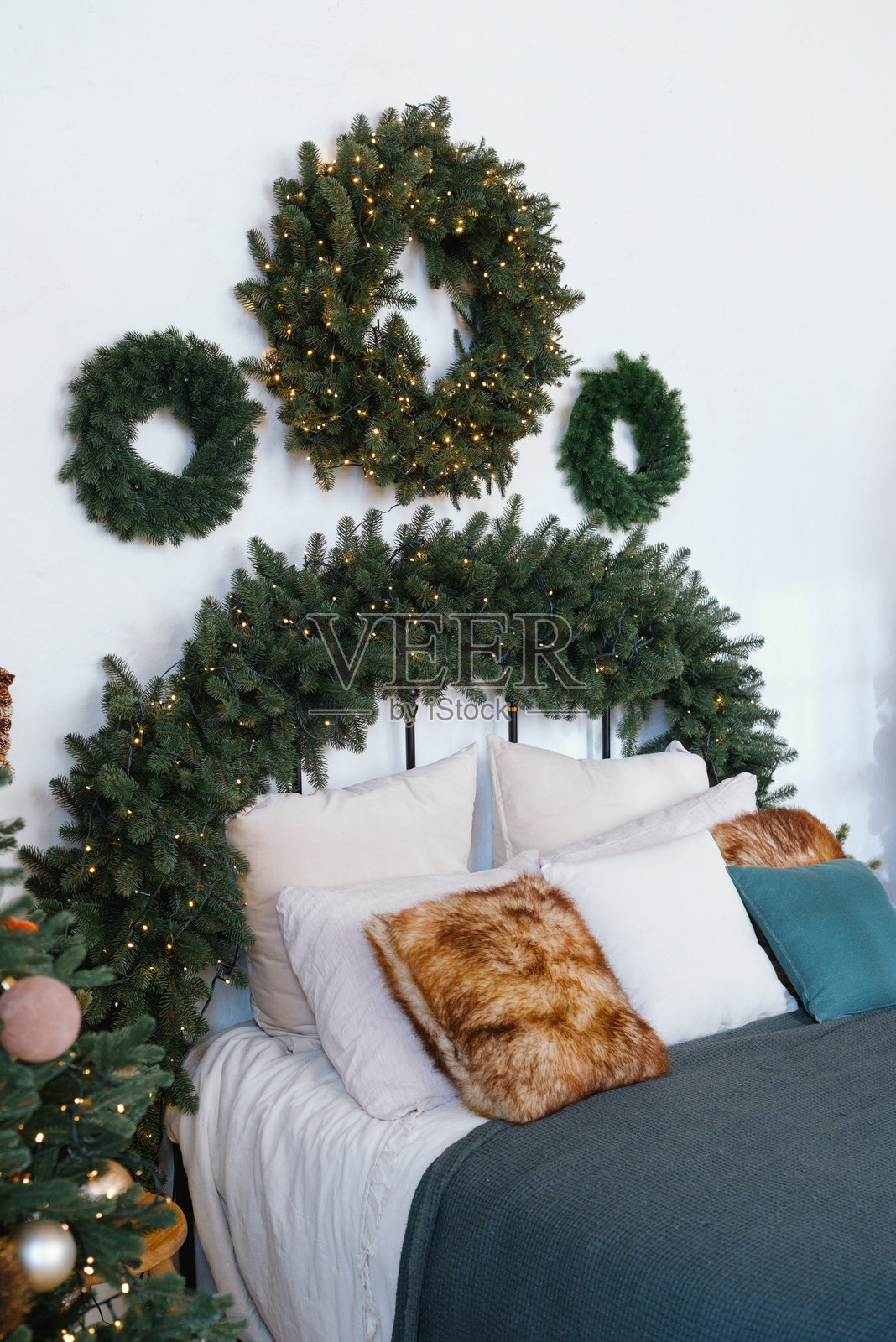 舒适的卧室，装饰着郁郁葱葱的绿色花环和点缀着温暖闪烁灯光的节日松树花环。照片摄影图片