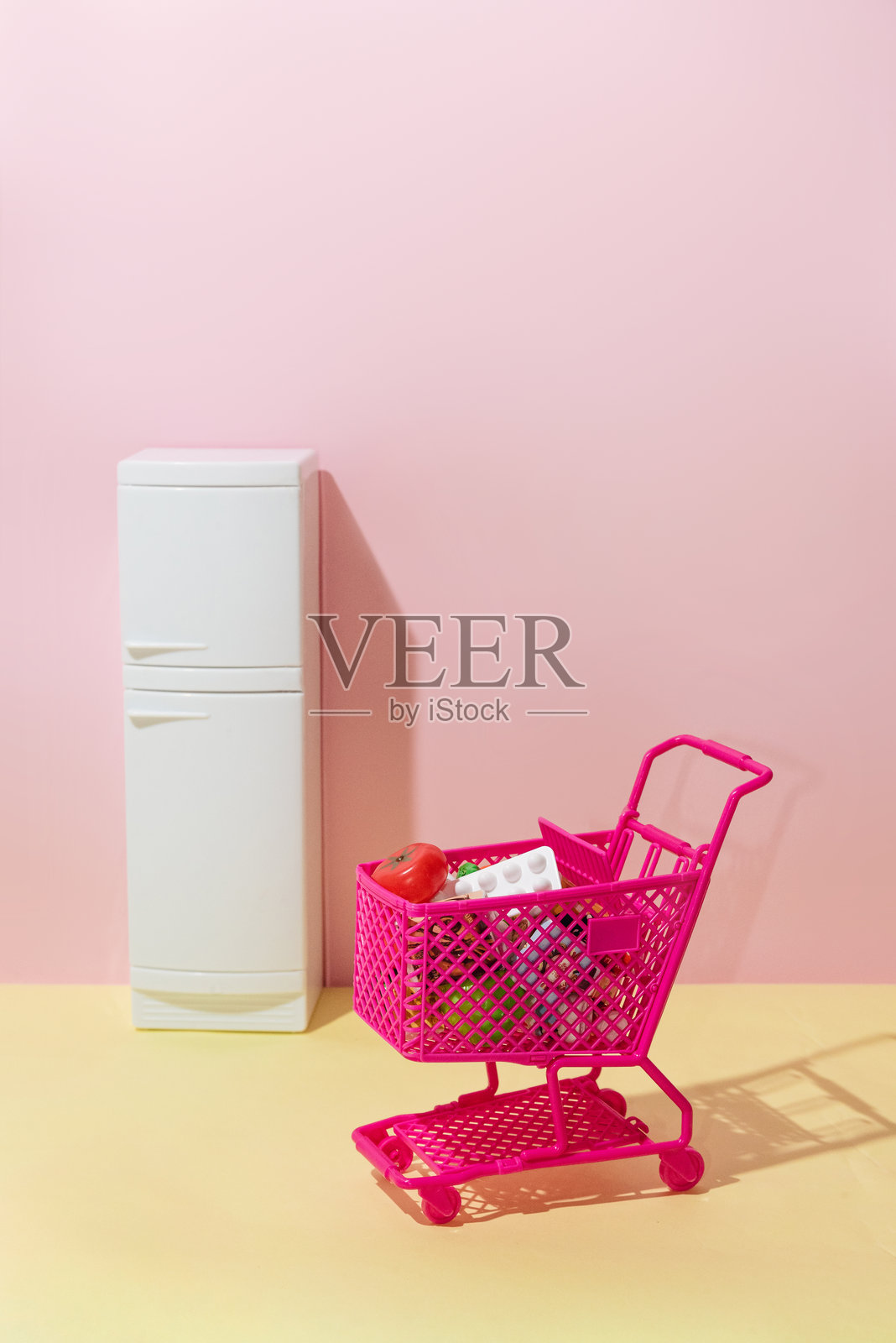 购物车的杂货篮和冰箱，黄色和粉色背景，创意照片摄影图片