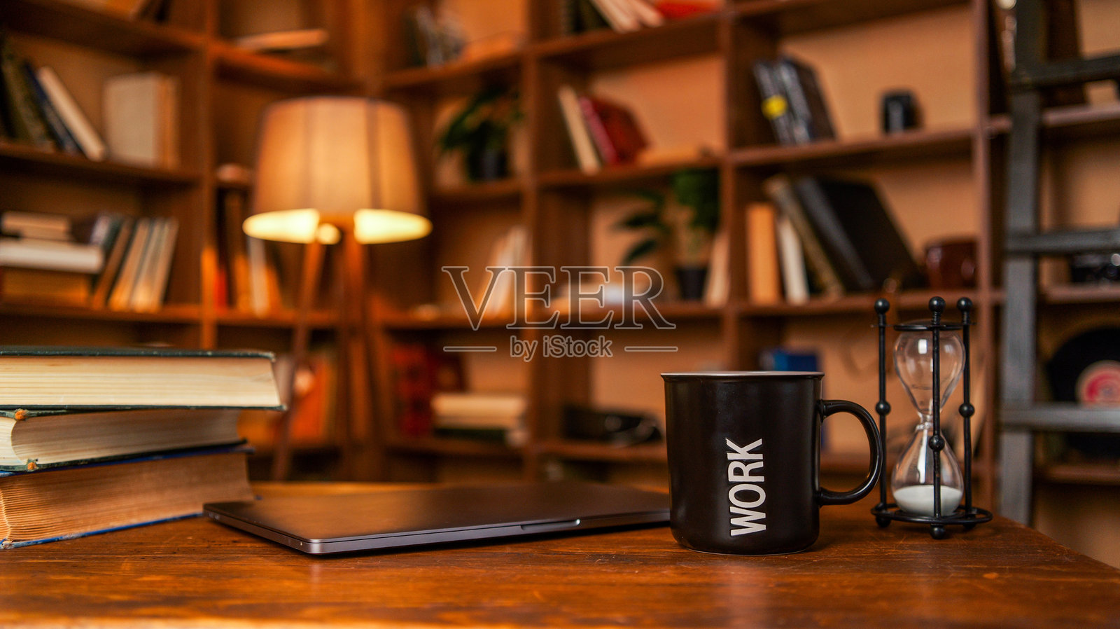 舒适的家庭办公室布置，木桌上放着书本、笔记本电脑、咖啡杯和沙漏照片摄影图片