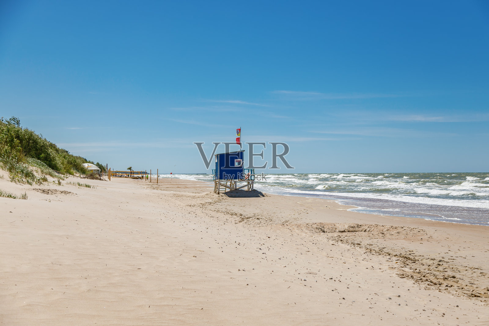 蓝色的救生员站台位于宽阔的沙滩上，海浪拍打着海岸，天空晴朗，象征着海岸安全概念。照片摄影图片