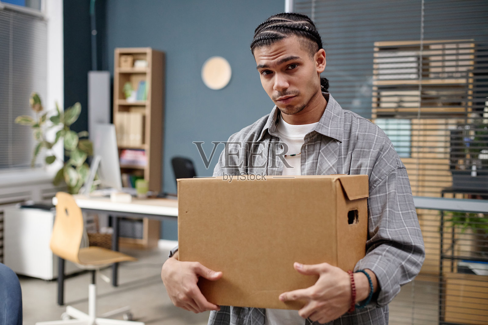 年轻成年黑人男性肖像，手持纸箱，置身于现代办公室照片摄影图片