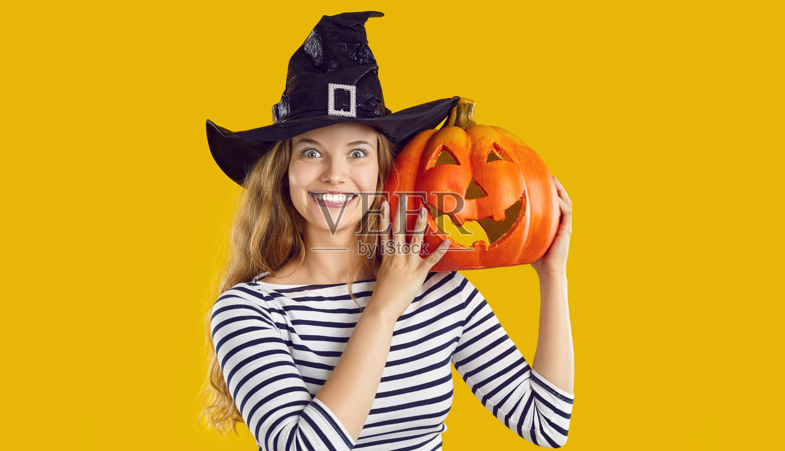 戴着女巫帽、手拿万圣节南瓜的快乐美丽年轻女子肖像照片摄影图片
