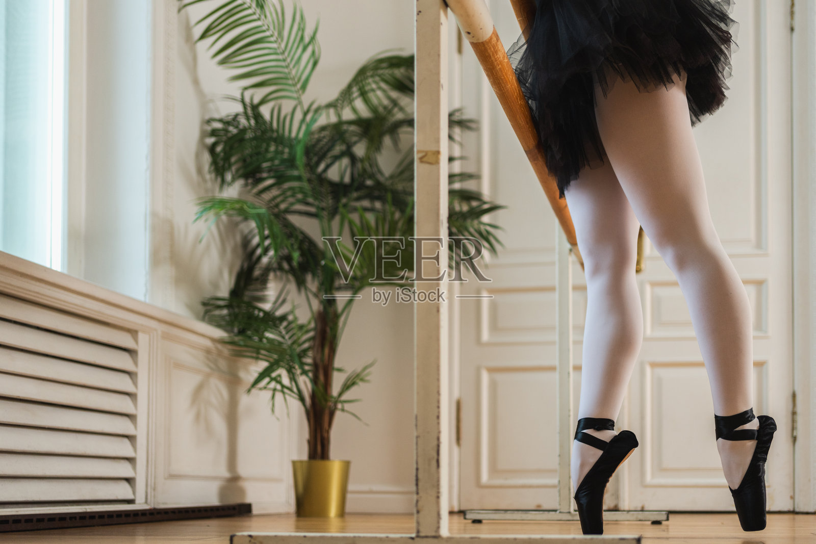 芭蕾舞演员在舞蹈教室里，在把杆旁练习芭蕾舞姿势，进行拉伸训练。特写脚穿足尖鞋的腿。古典舞女演员在练舞房。芭蕾舞课训练，芭蕾舞学校。照片摄影图片