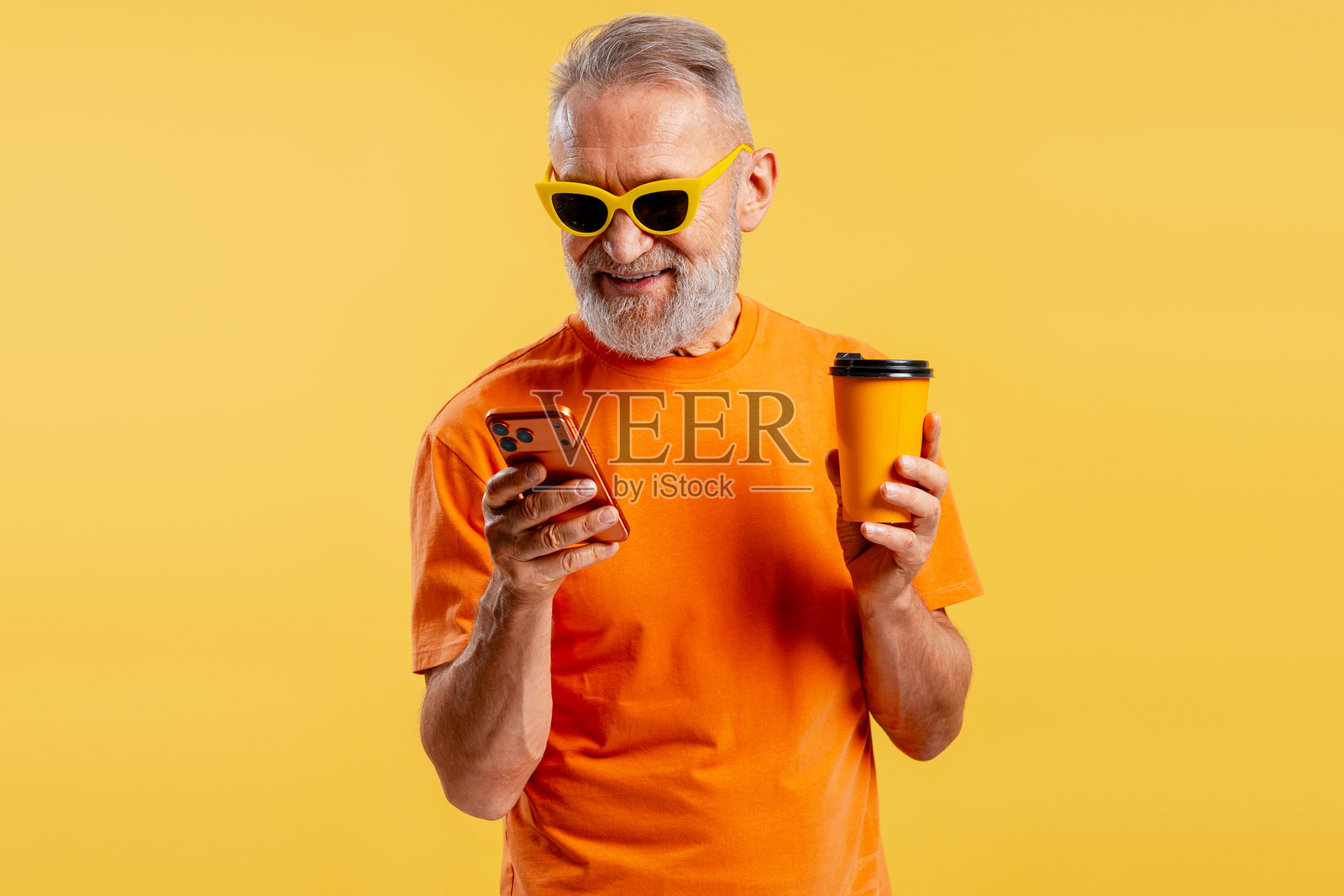 一位老人微笑着，手持黄色杯子，正在使用手机，背景为黄色，上面有短信内容。照片摄影图片