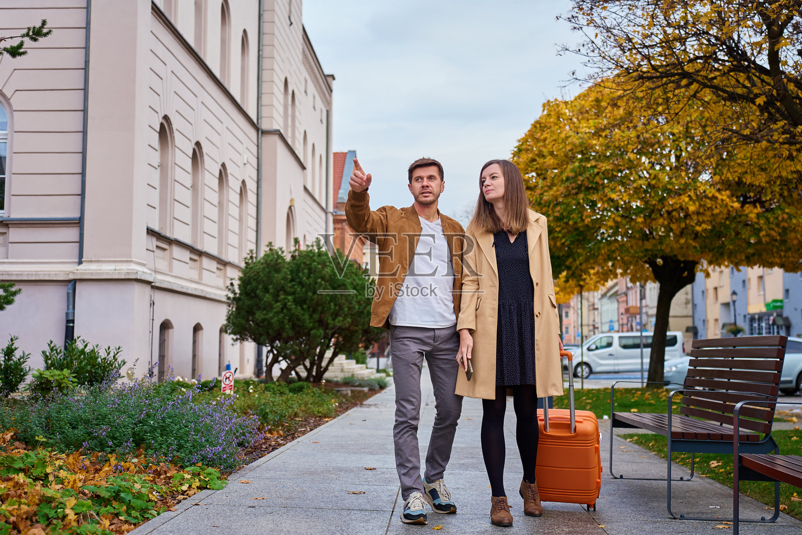 男人和女人拖着行李箱走在城市人行道上，男人正在指明方向照片摄影图片