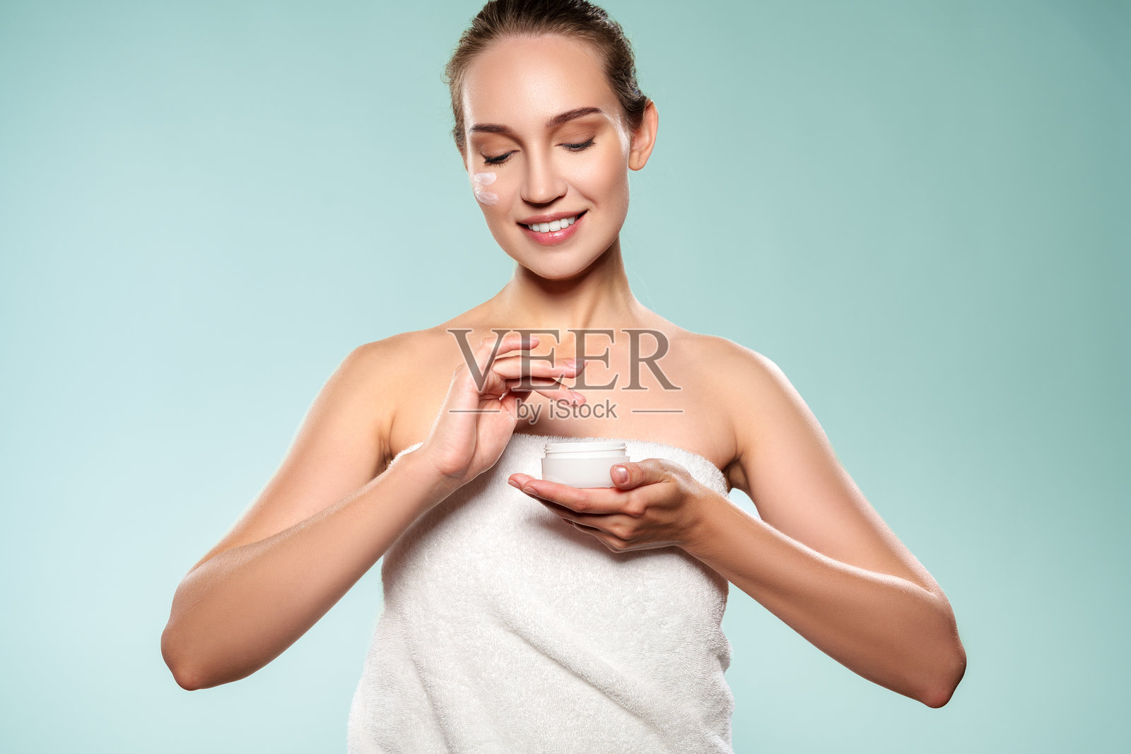 一位女性在光线充足的环境中，背景简洁，她一手拿着罐子，一手涂抹着面霜照片摄影图片