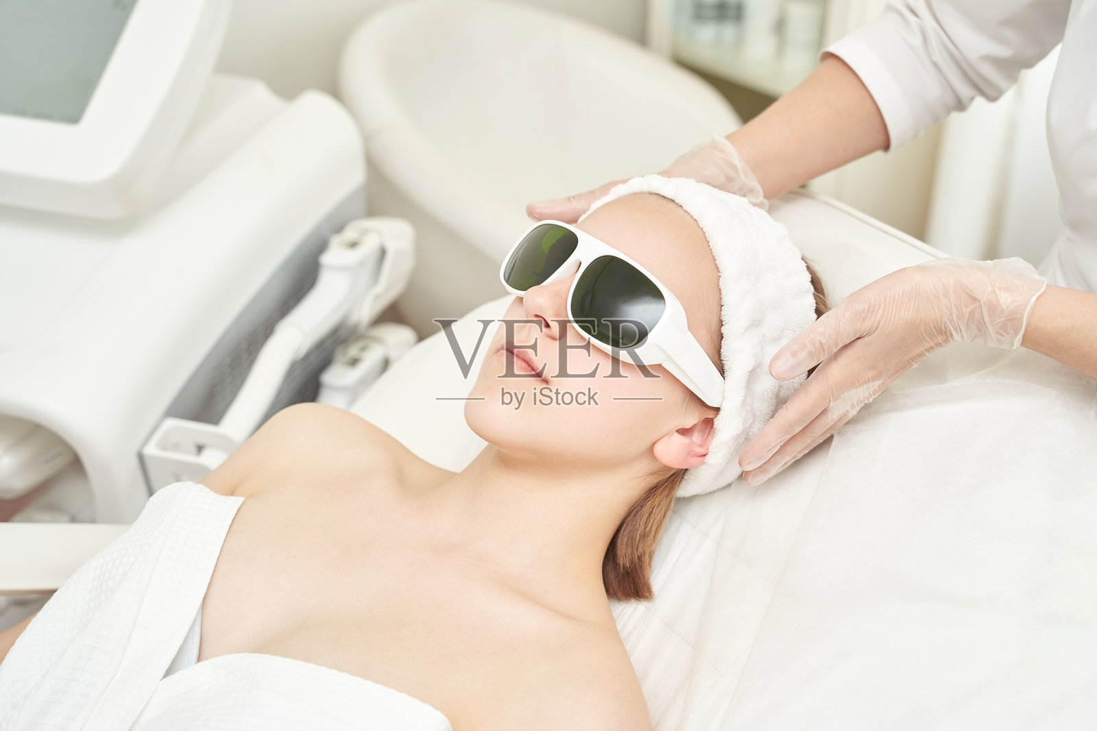 年轻的白种女性在水疗中心佩戴激光护目镜接受面部护理照片摄影图片