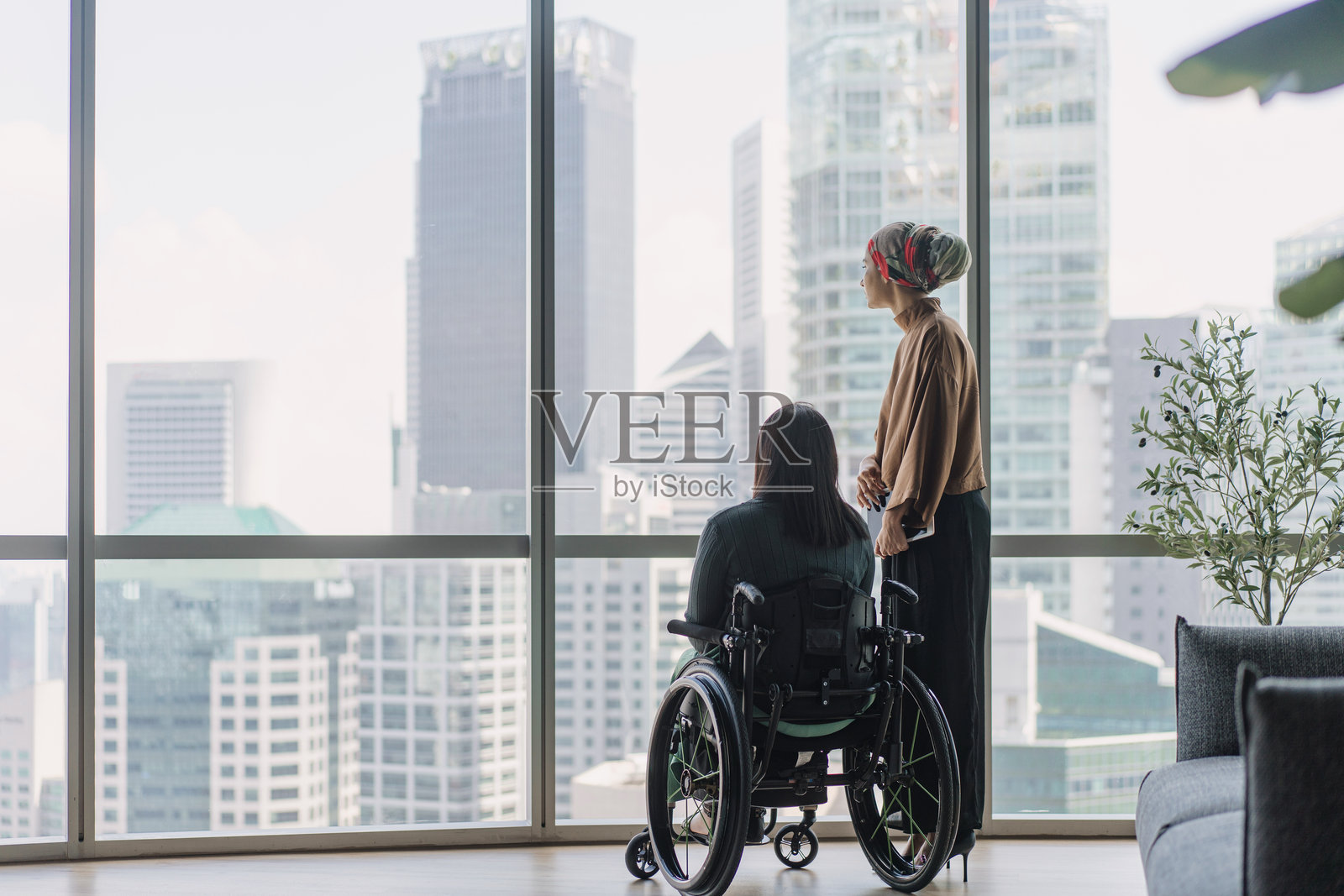 一对亚洲高管，其中一位坐在轮椅上，正在望着办公室窗外。照片摄影图片