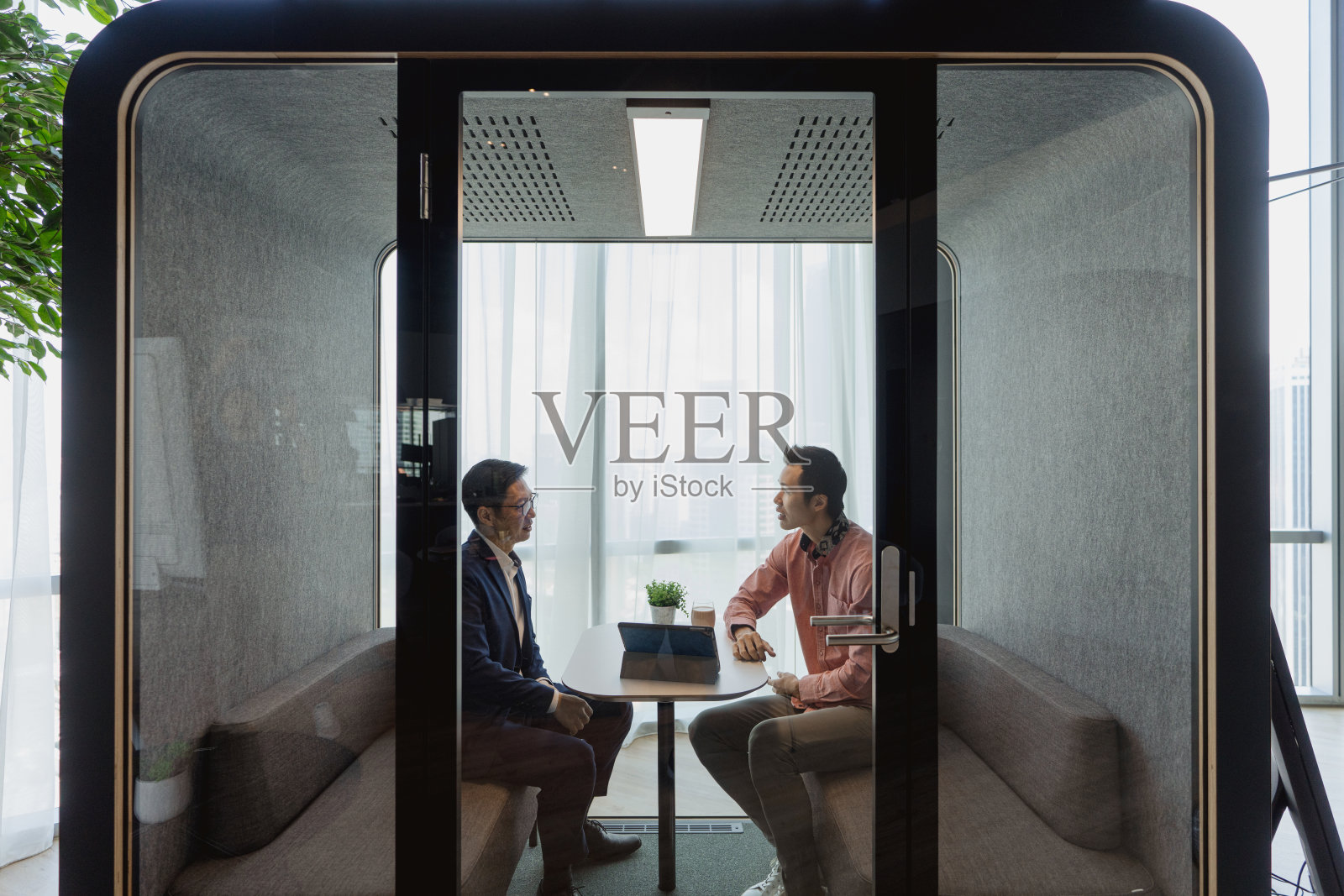 在办公室的隔音舱内，两位亚洲男性同事进行私人商务讨论照片摄影图片